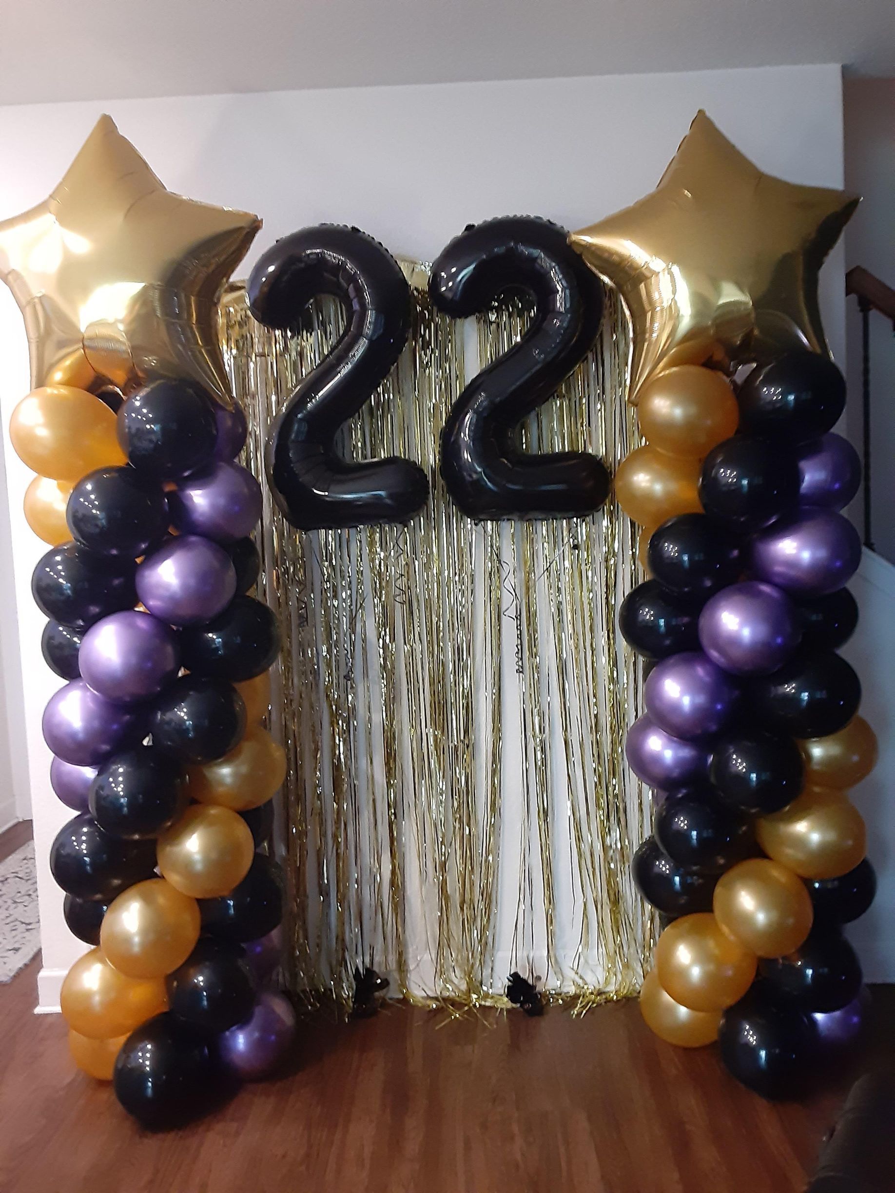 A gold, purple, and black balloon display with the number 22 on a gold fringe backdrop