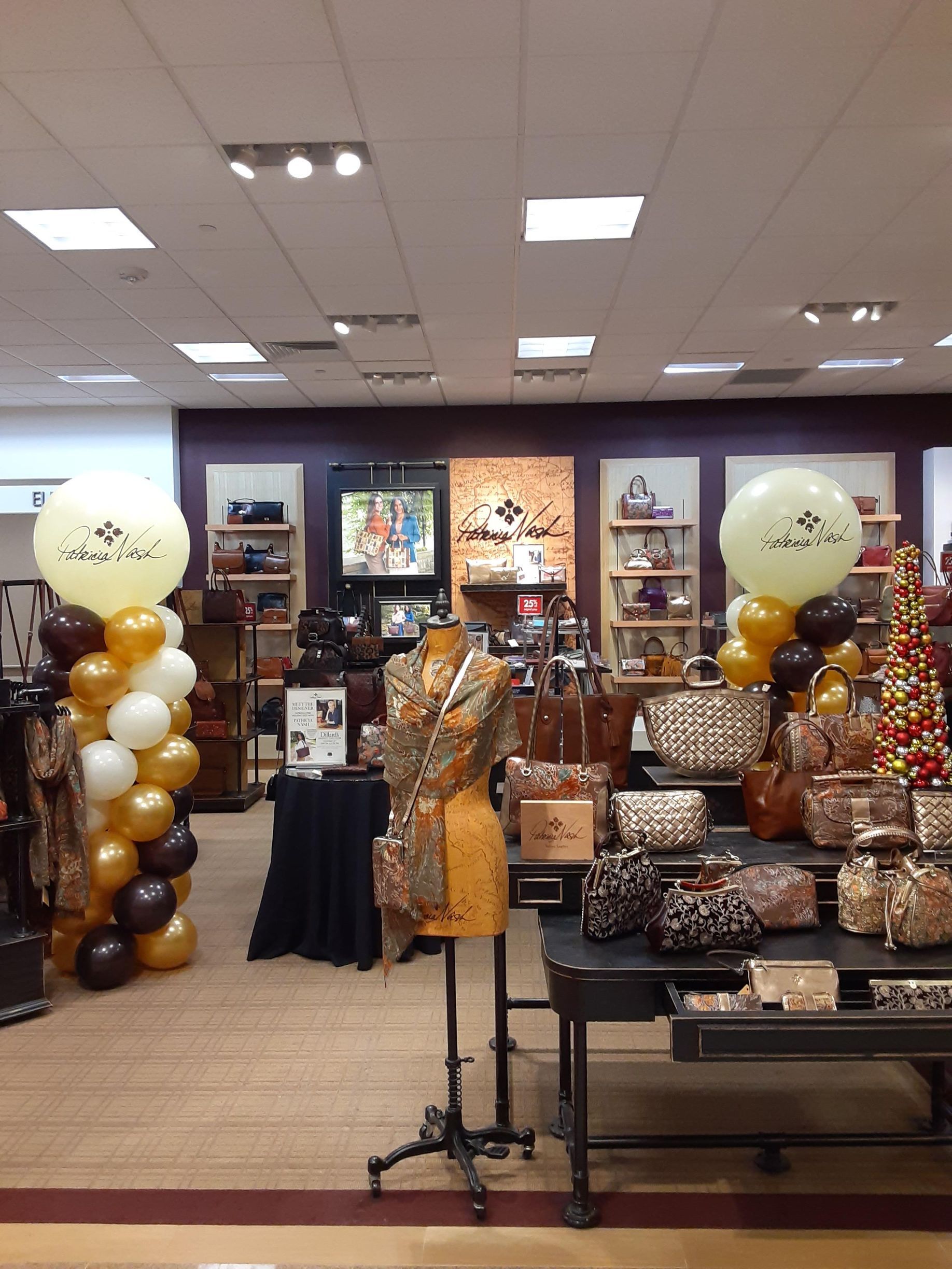 Display of merchandise in a store. Balloons, a mannequin, and handbags in shades of brown and gold are featured.
