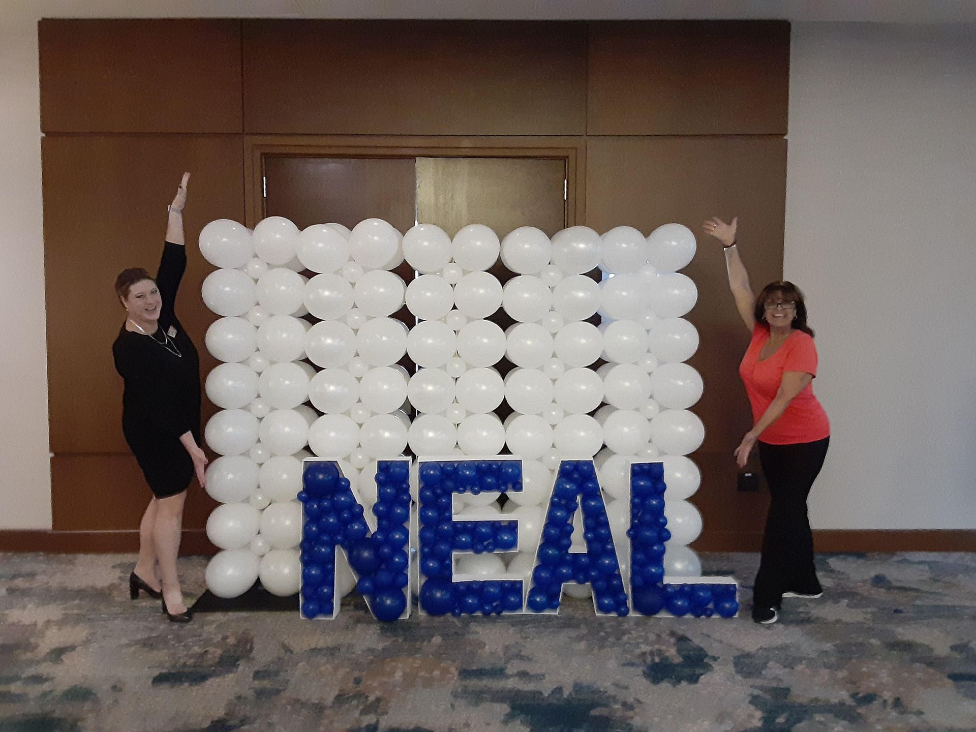 Two women standing in front of a wall made of balloons that says neal