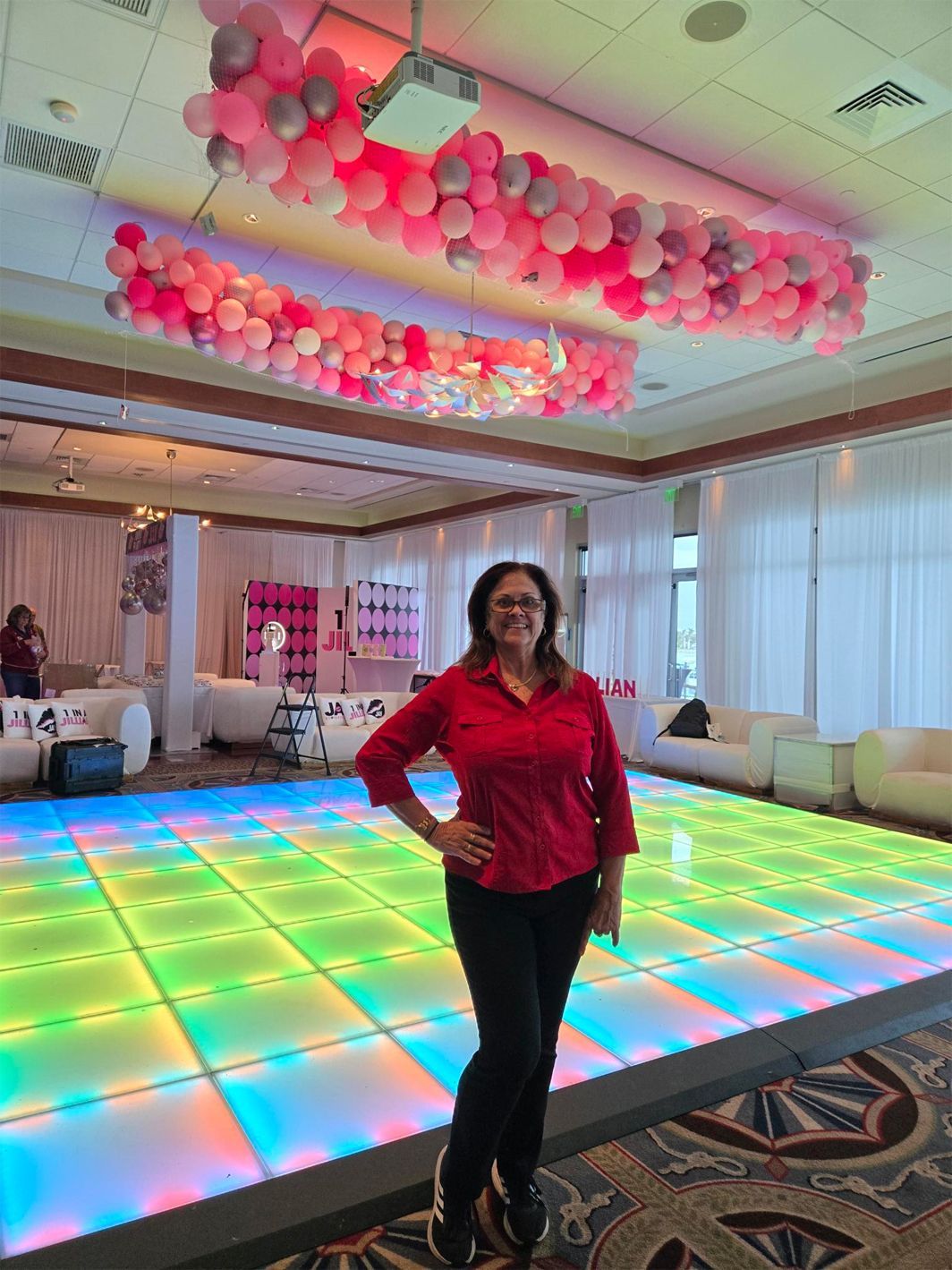 A woman is standing in front of a dance floor with balloons on the ceiling.