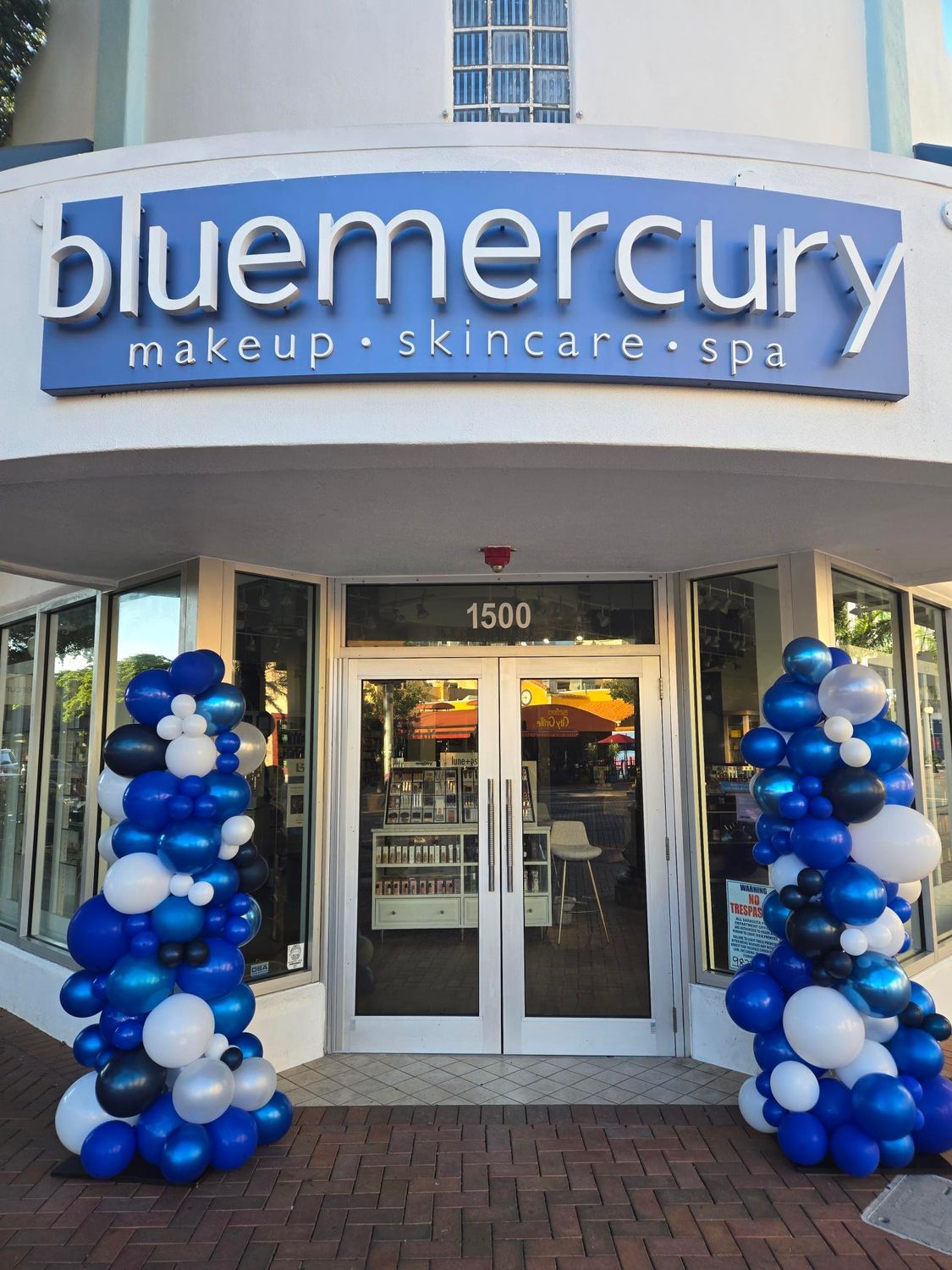 Blue Mercury storefront with blue balloons, white building, and glass doors.