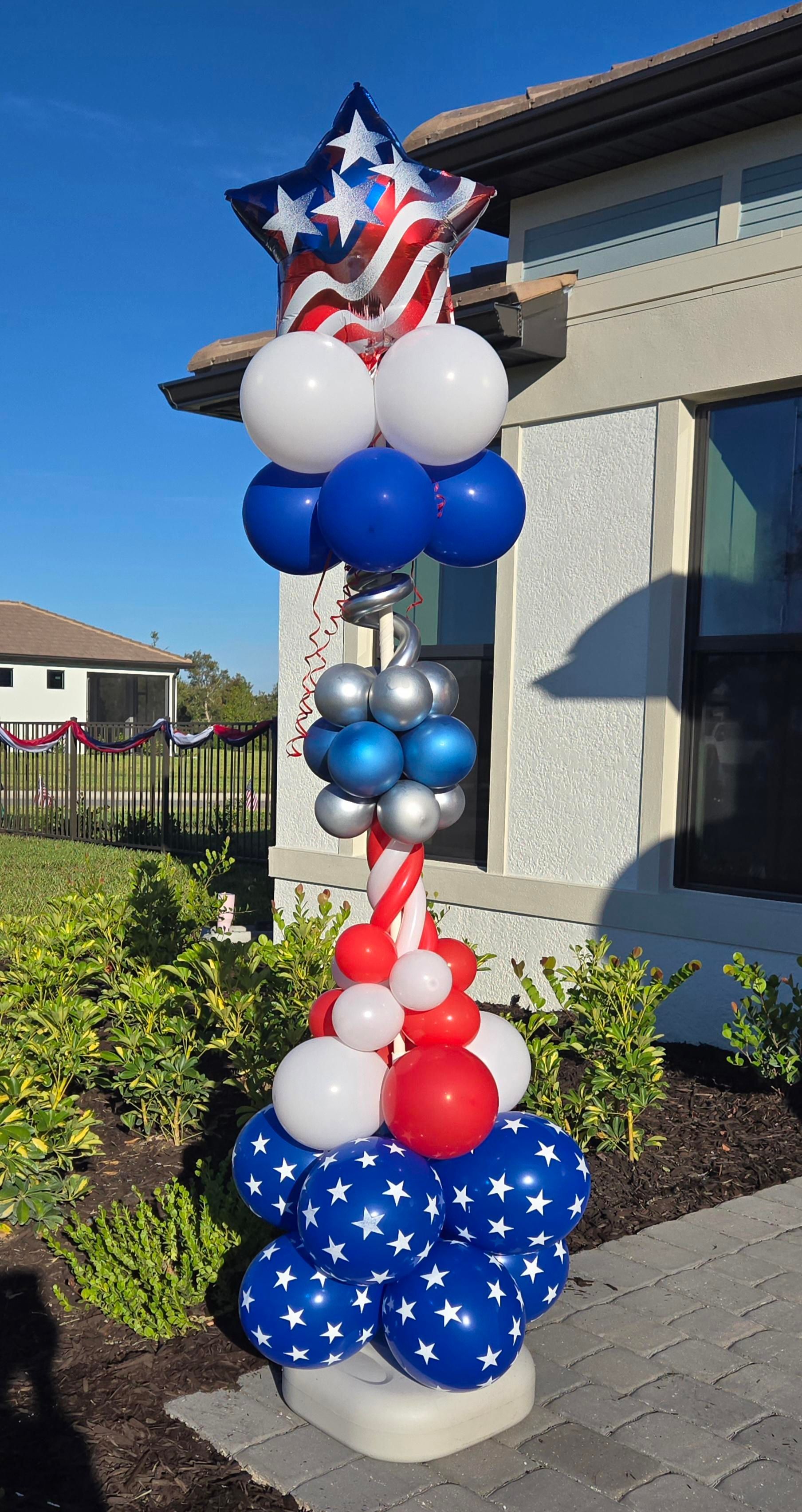A patriotic balloon column with red, white, and blue balloons, topped with a star-shaped American flag balloon