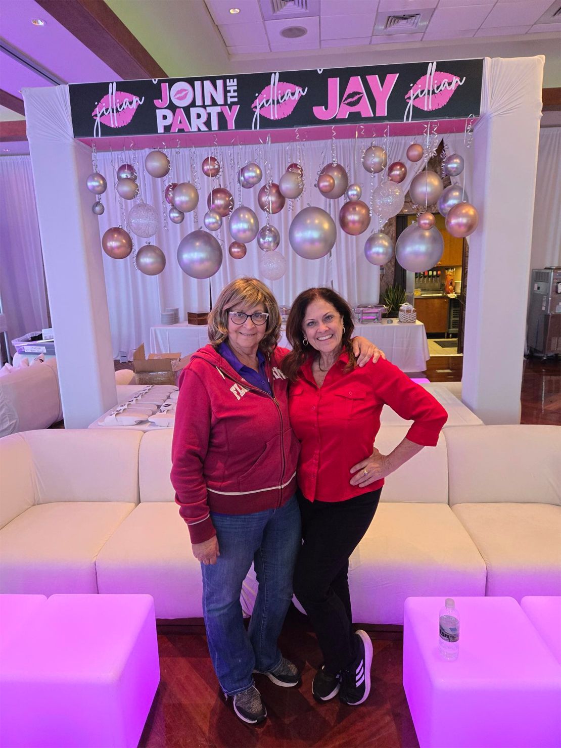 Two women are posing for a picture in front of a sign that says join the party.