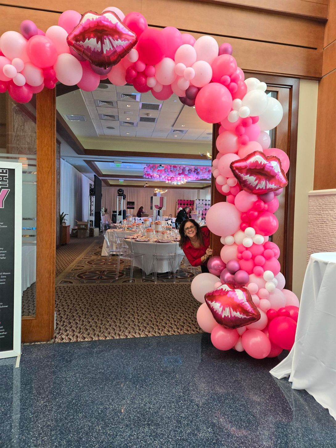 A woman is standing in front of a pink balloon arch.
