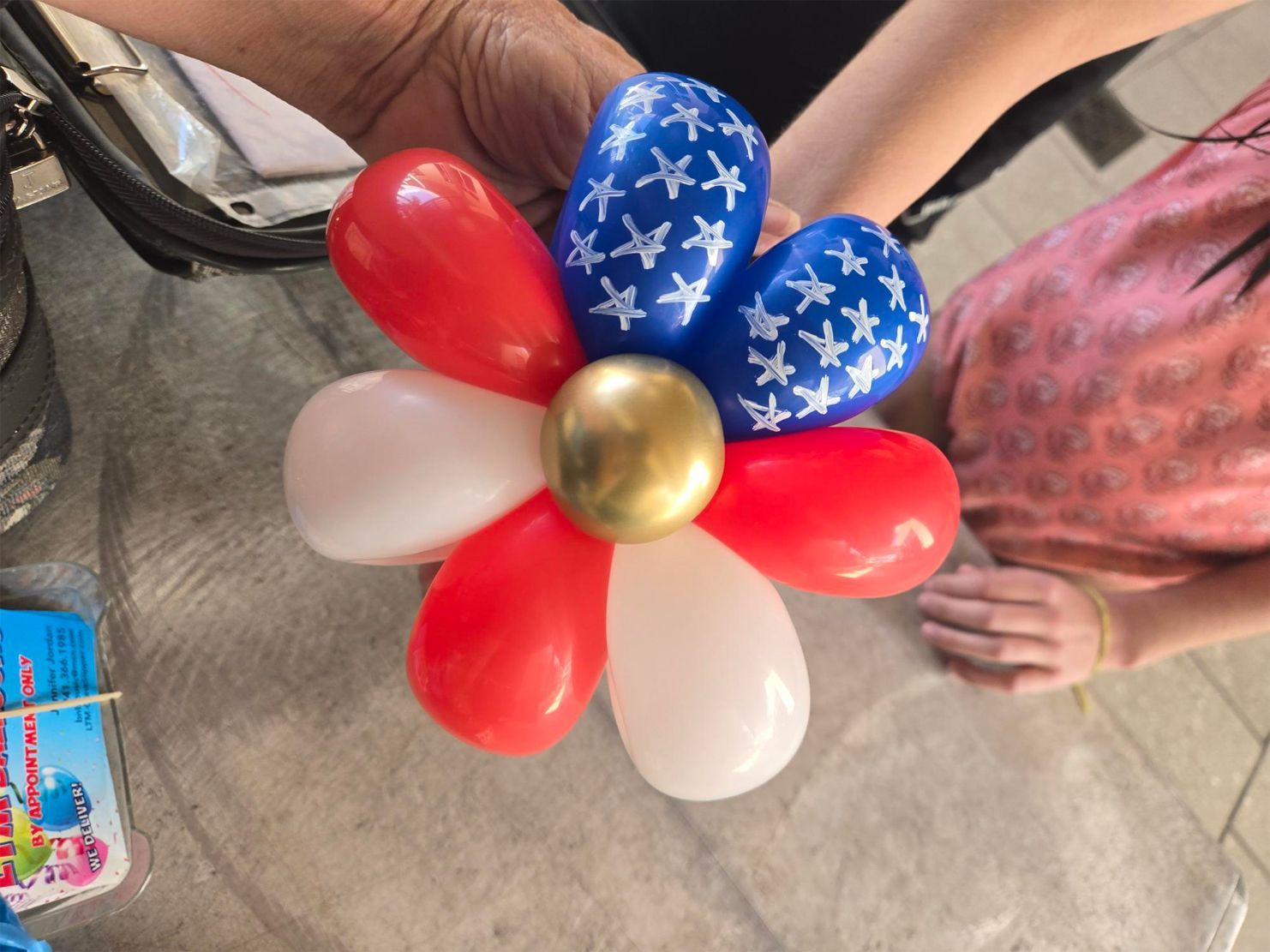 A person is holding a flower made of red white and blue balloons