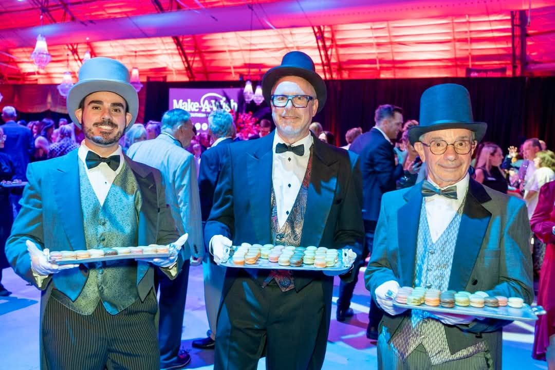 Three men in formal attire carrying trays of food at an event.