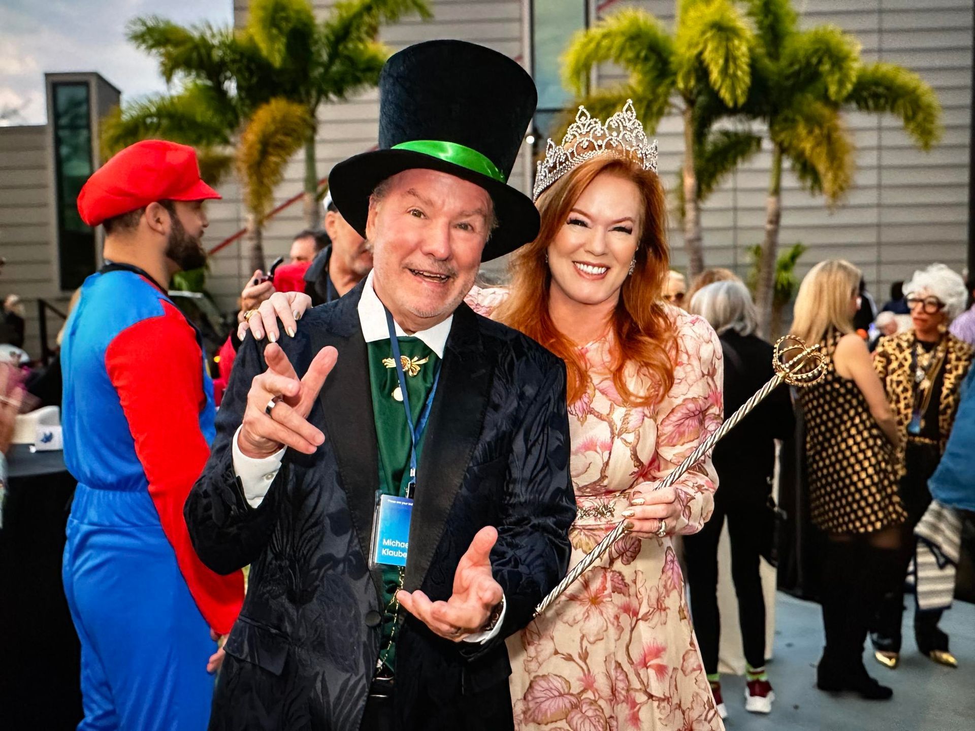 Man in top hat with woman in a crown, smiling at the camera. People in costume, outdoor setting.