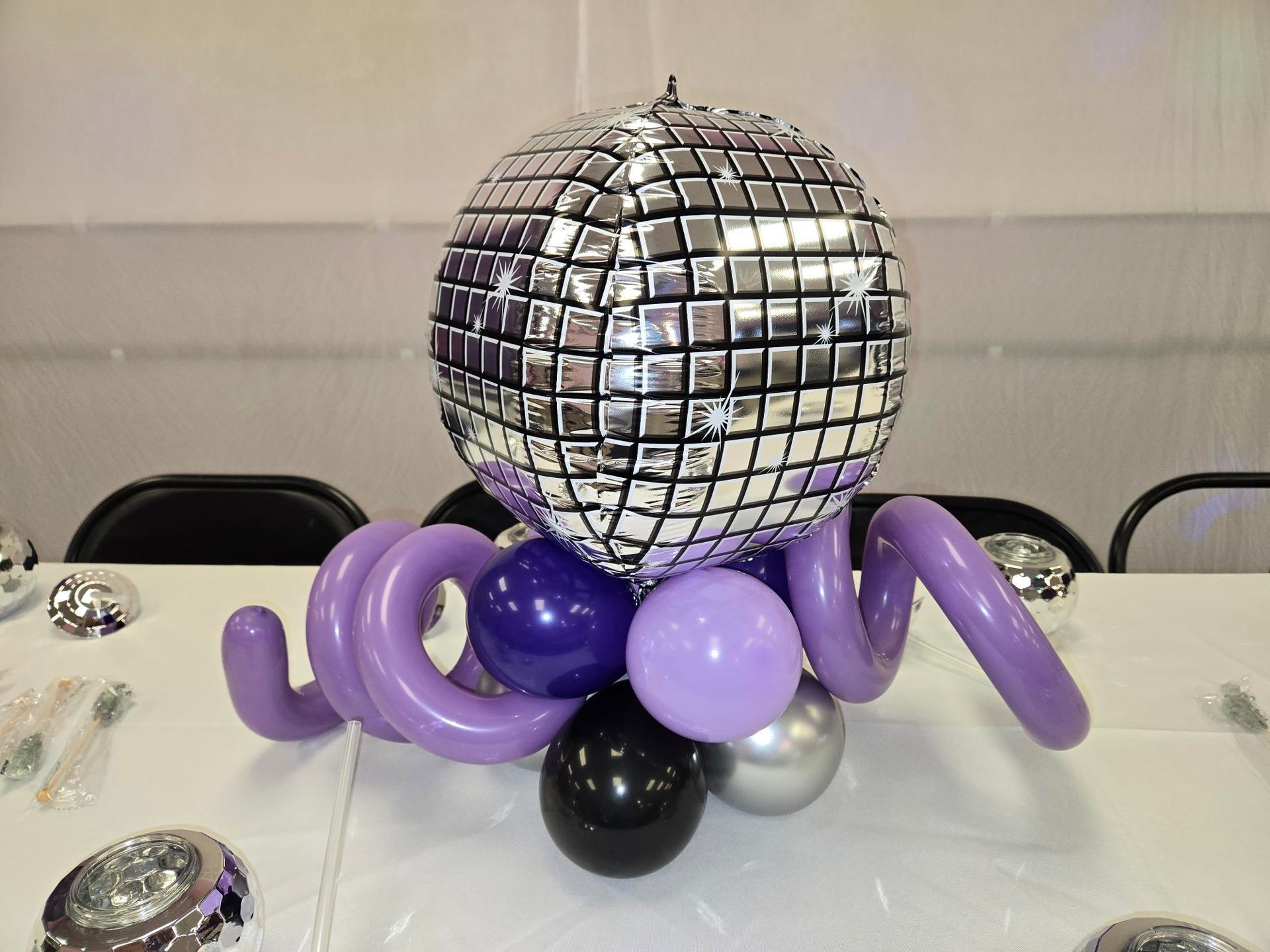 Disco ball centerpiece with purple, black, and silver balloons on a white table