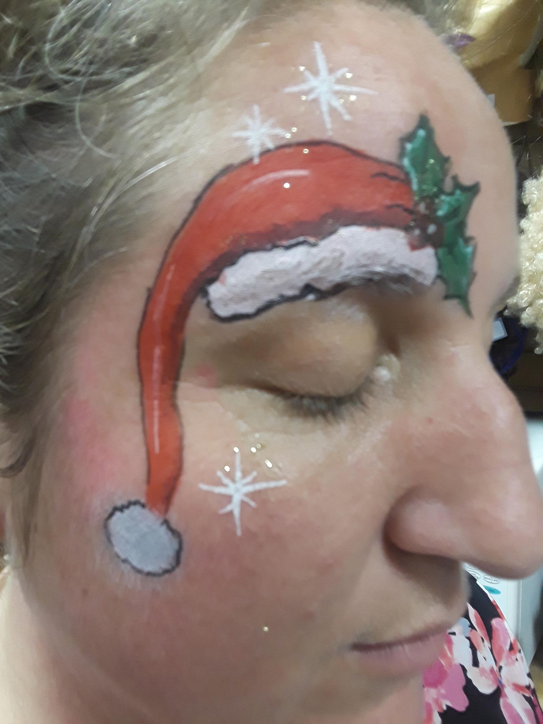 Person with face paint of a Santa hat with holly and white stars