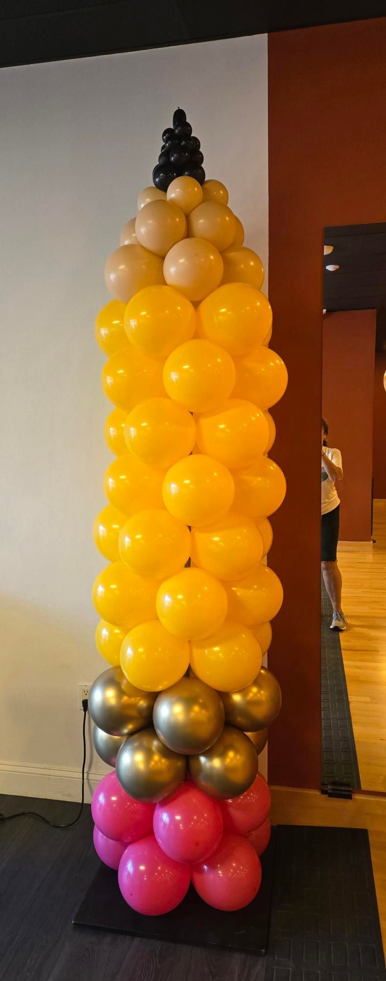 A large pencil made of balloons, standing on a black mat. The 
