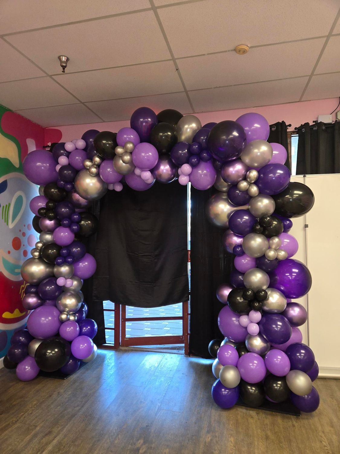 Purple, black, and silver balloon archway frames a doorway in a room