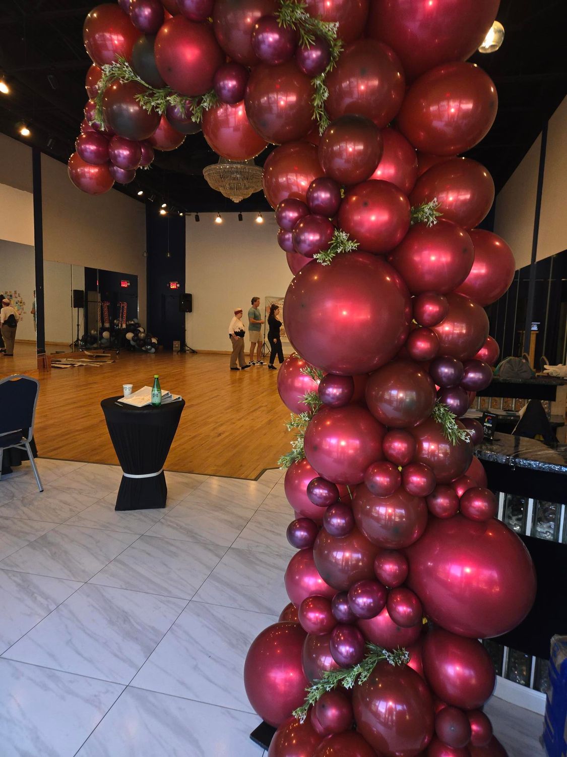 Archway decorated with maroon balloons and greenery inside a dance studio