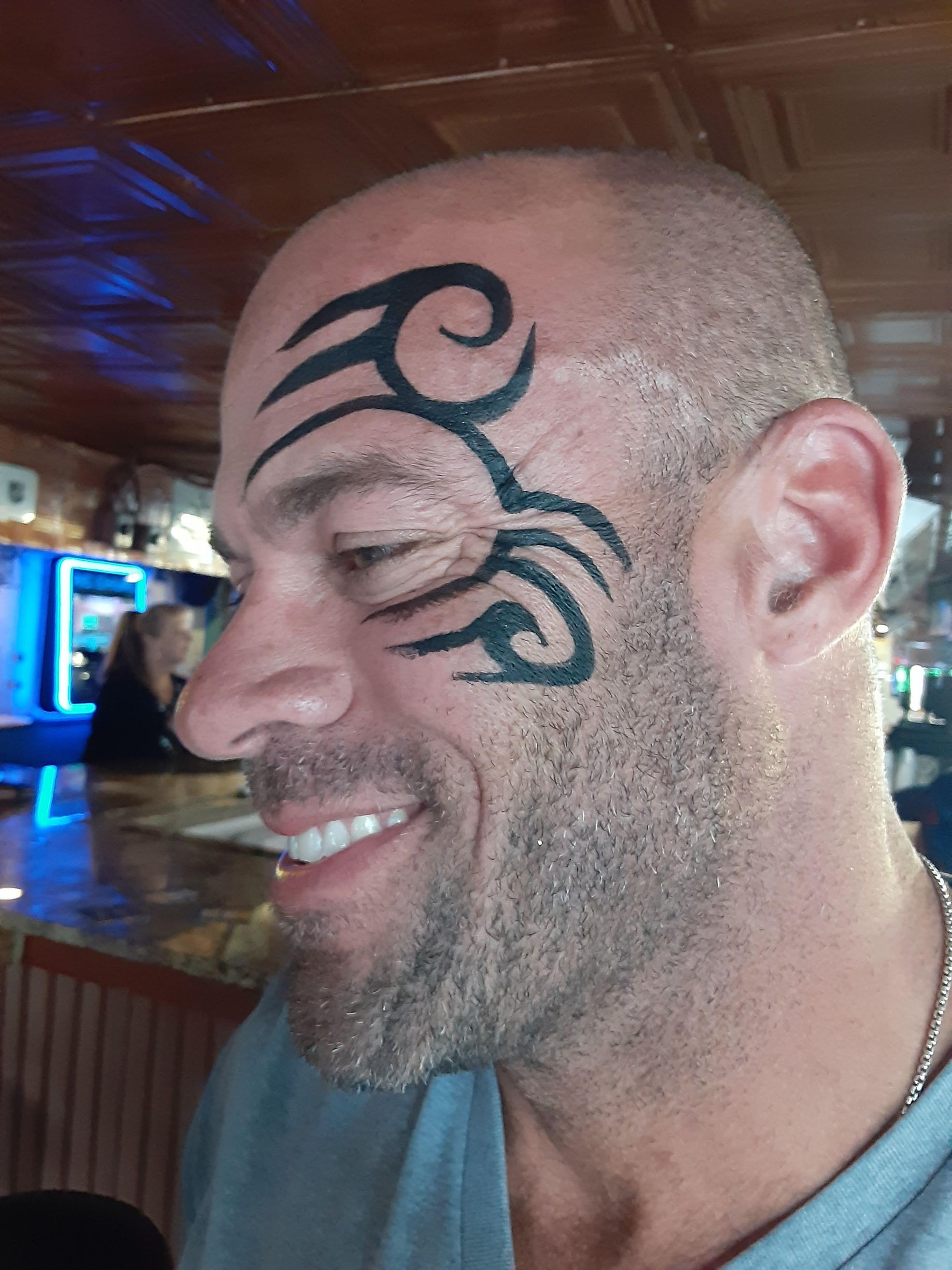 Man with shaved head and face tattoo smiling