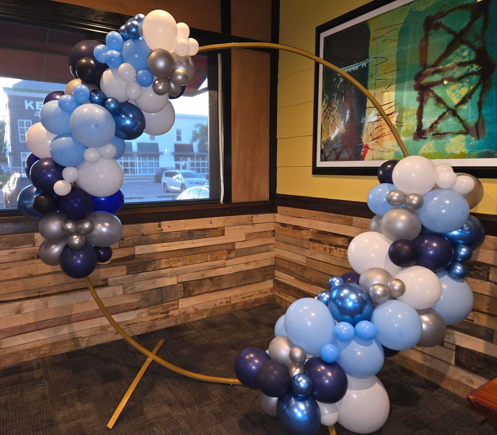 A gold circular balloon arch decorated with blue, white, and silver balloons inside a restaurant