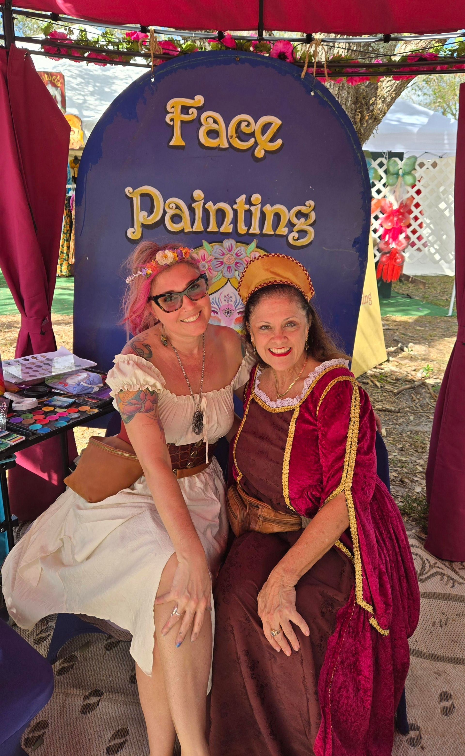 Two women dressed in Renaissance costumes at a face painting booth