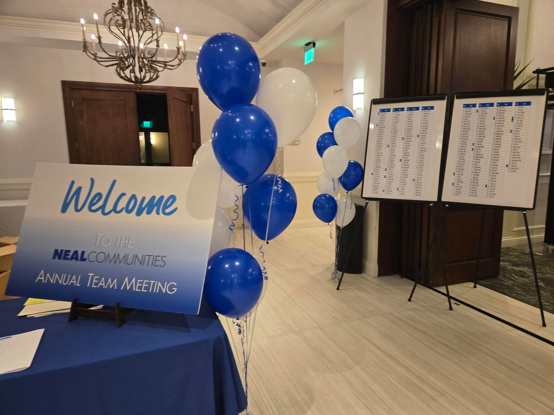 Entrance to an event with welcome sign, balloons, and seating charts