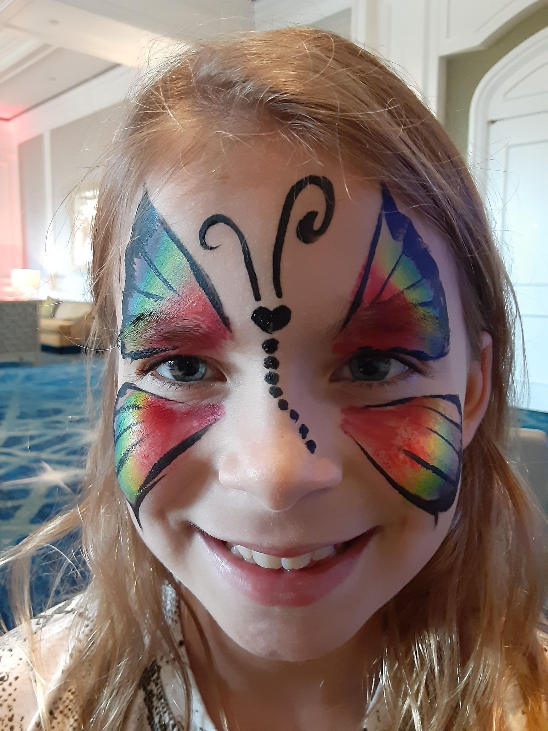Girl with rainbow butterfly face paint smiles