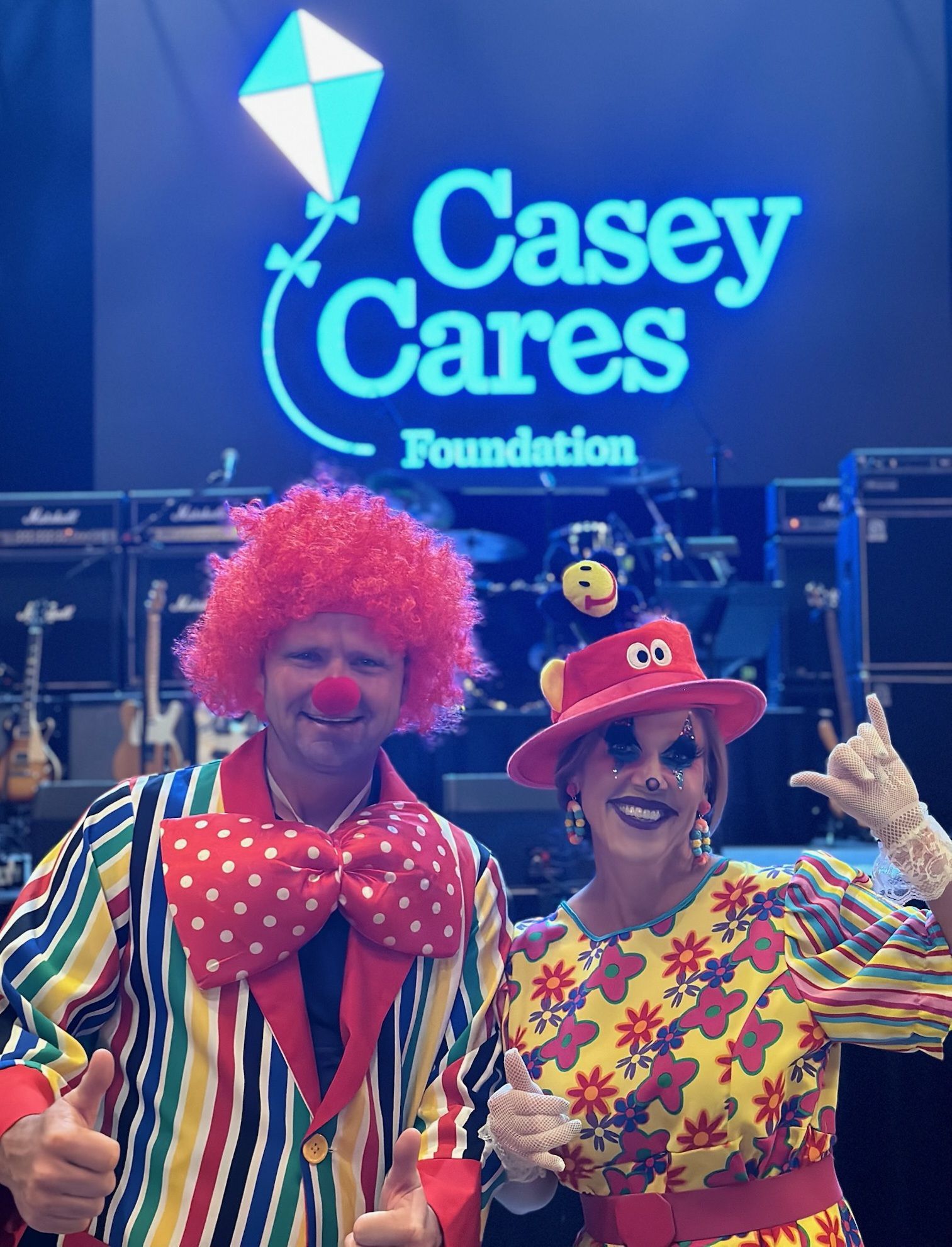 Two clowns in costume pose in front of a 