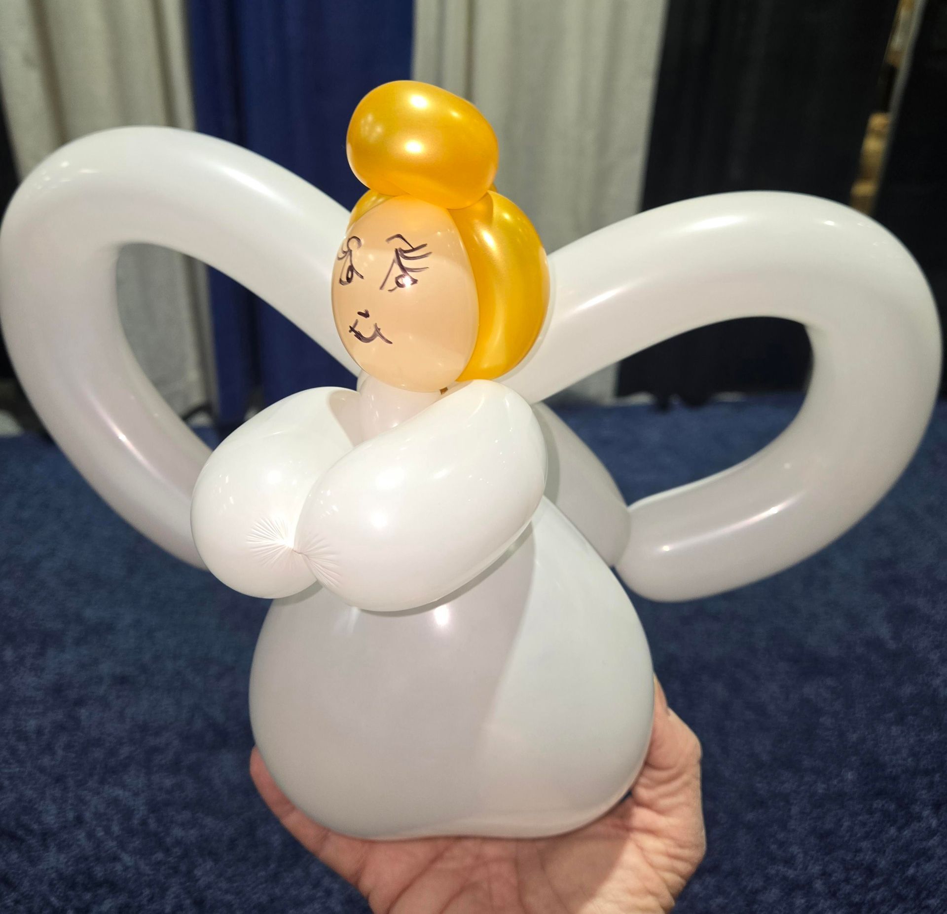 Balloon angel with white body and wings, yellow hair, and drawn facial features.