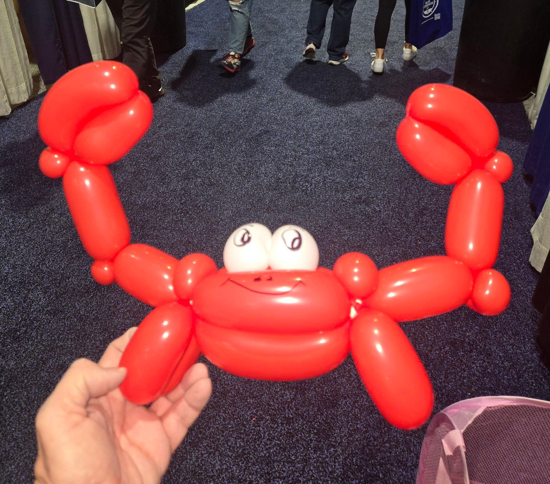 Red balloon crab sculpture with large claws and googly eyes. Hand holding near legs.