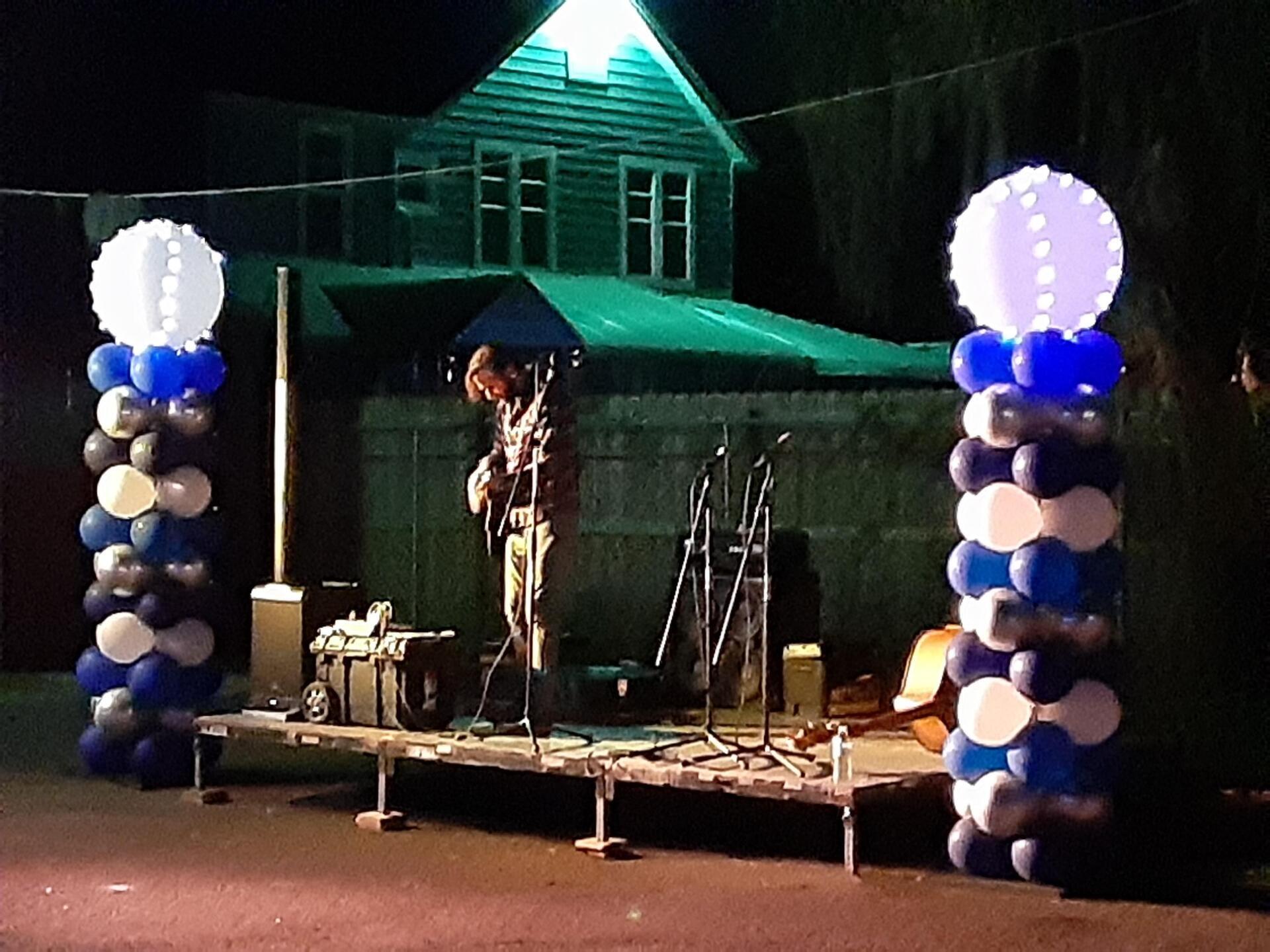 A man playing a guitar on a stage surrounded by blue and white balloons