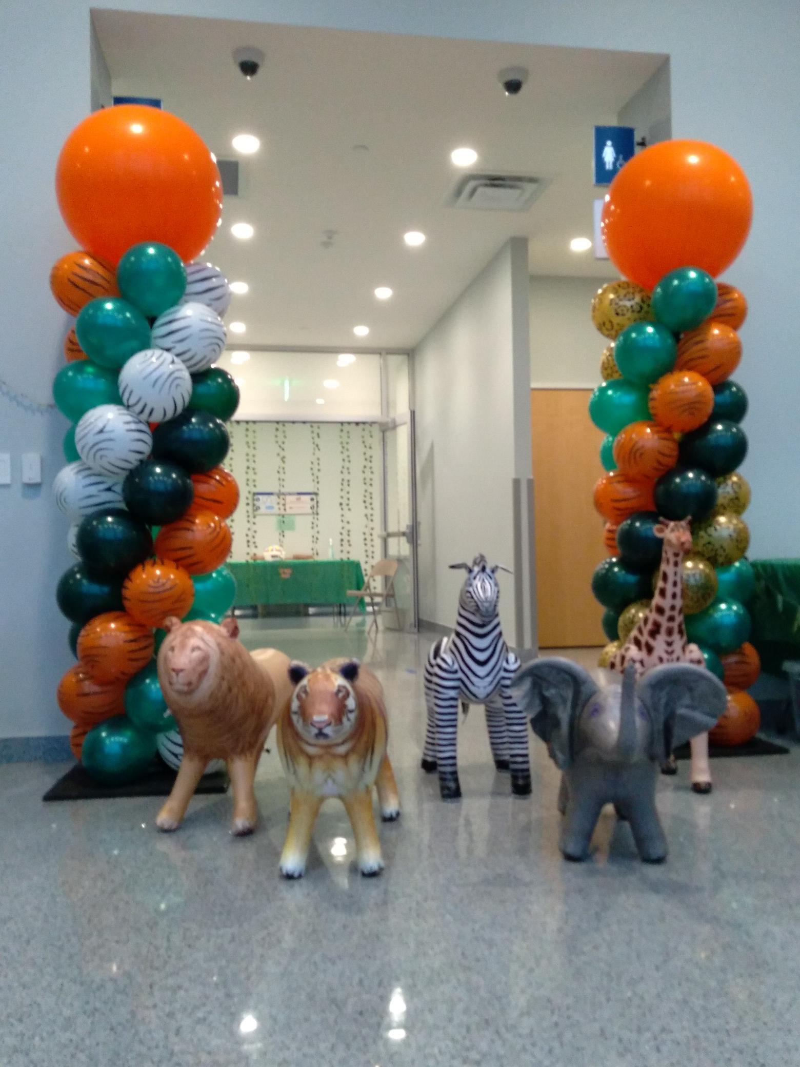A group of stuffed animals are standing in front of balloons in a hallway.
