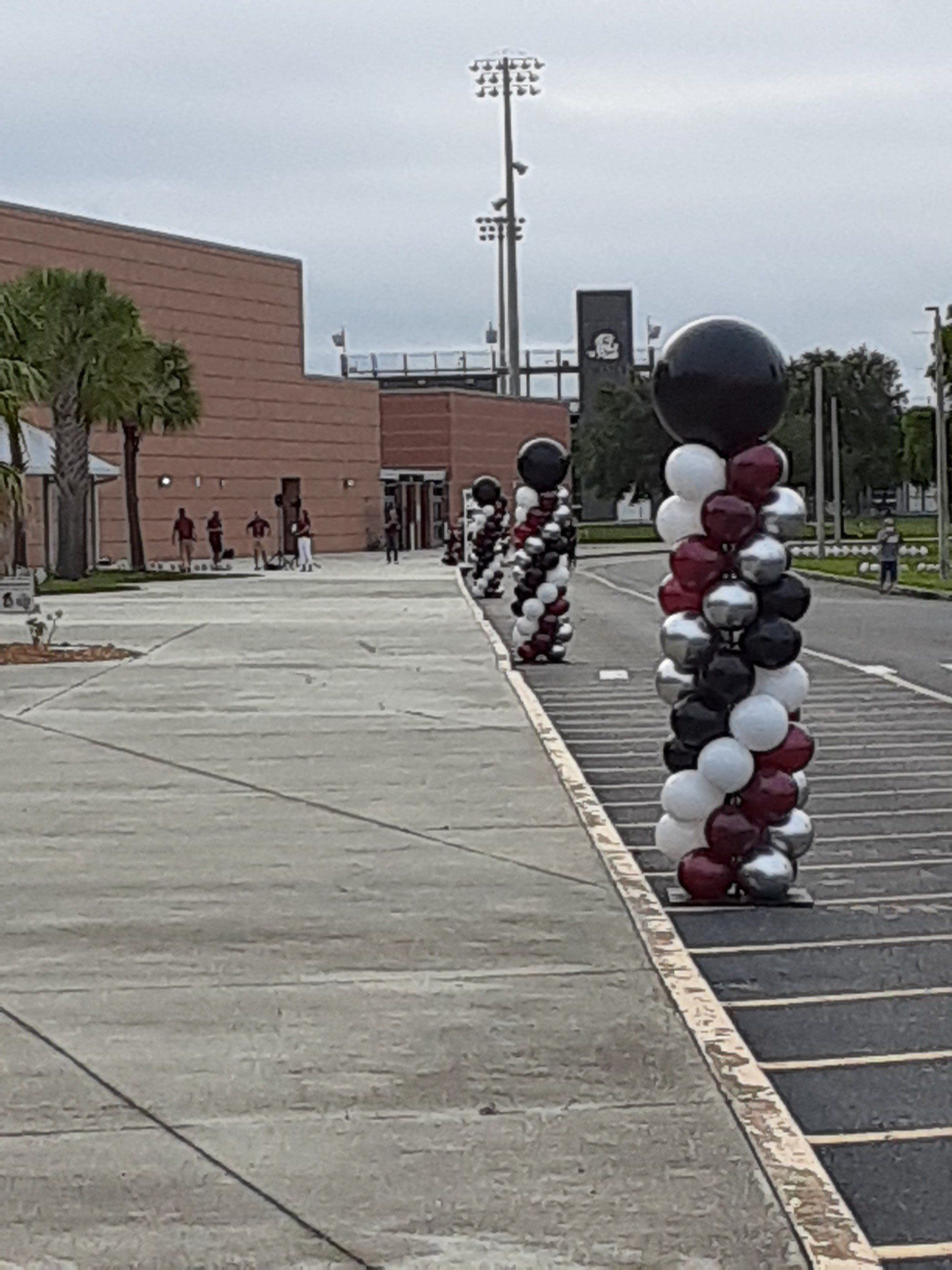 A row of balloons are lined up in a parking lot in front of a building.