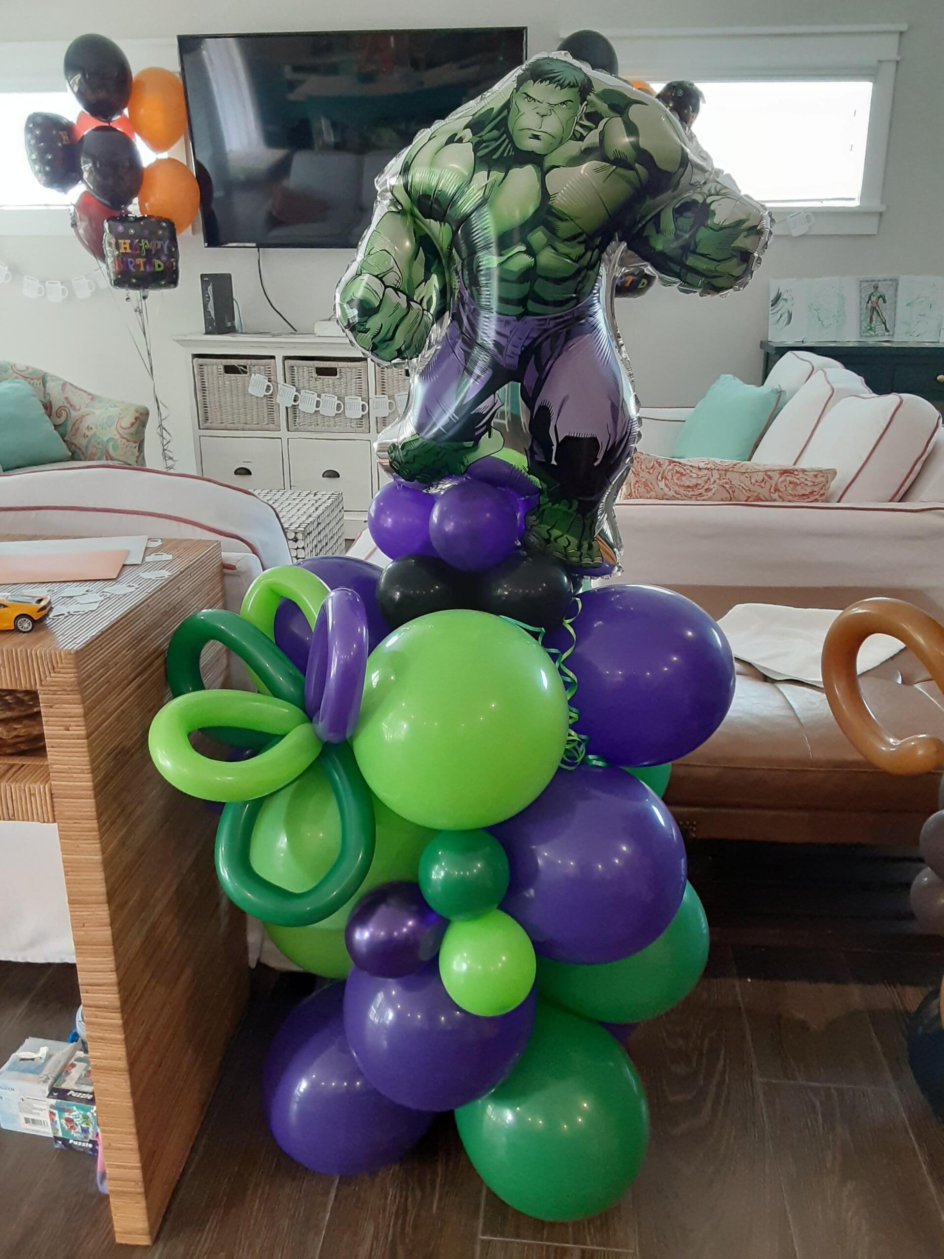A hulk balloon is sitting on top of a bunch of balloons in a living room.