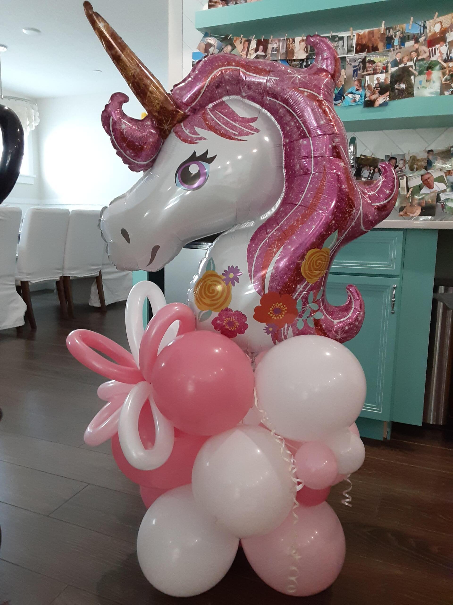 A unicorn balloon is sitting on top of a bunch of pink and white balloons.