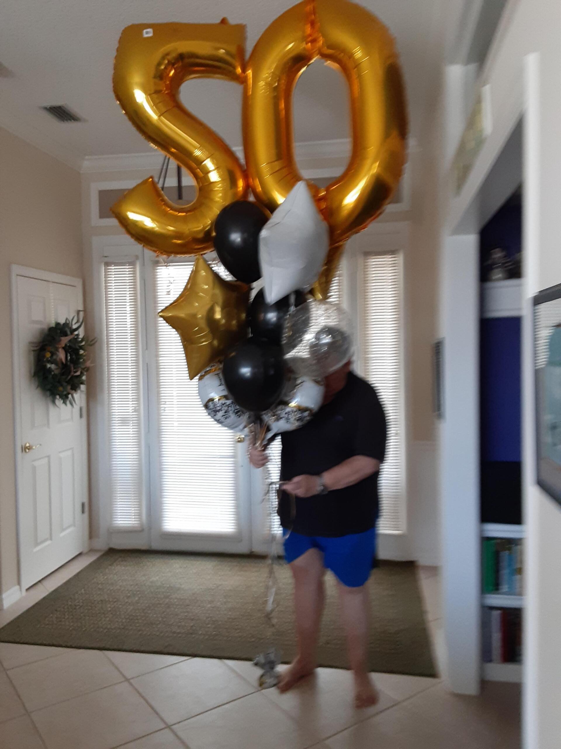 A man is holding a bunch of balloons with the number 50 on them