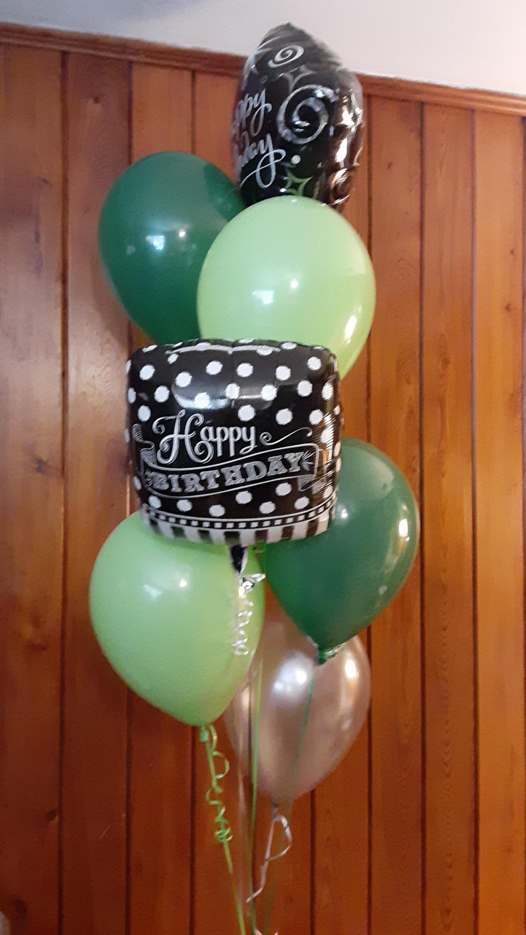 A bunch of green and silver balloons on a wooden wall.