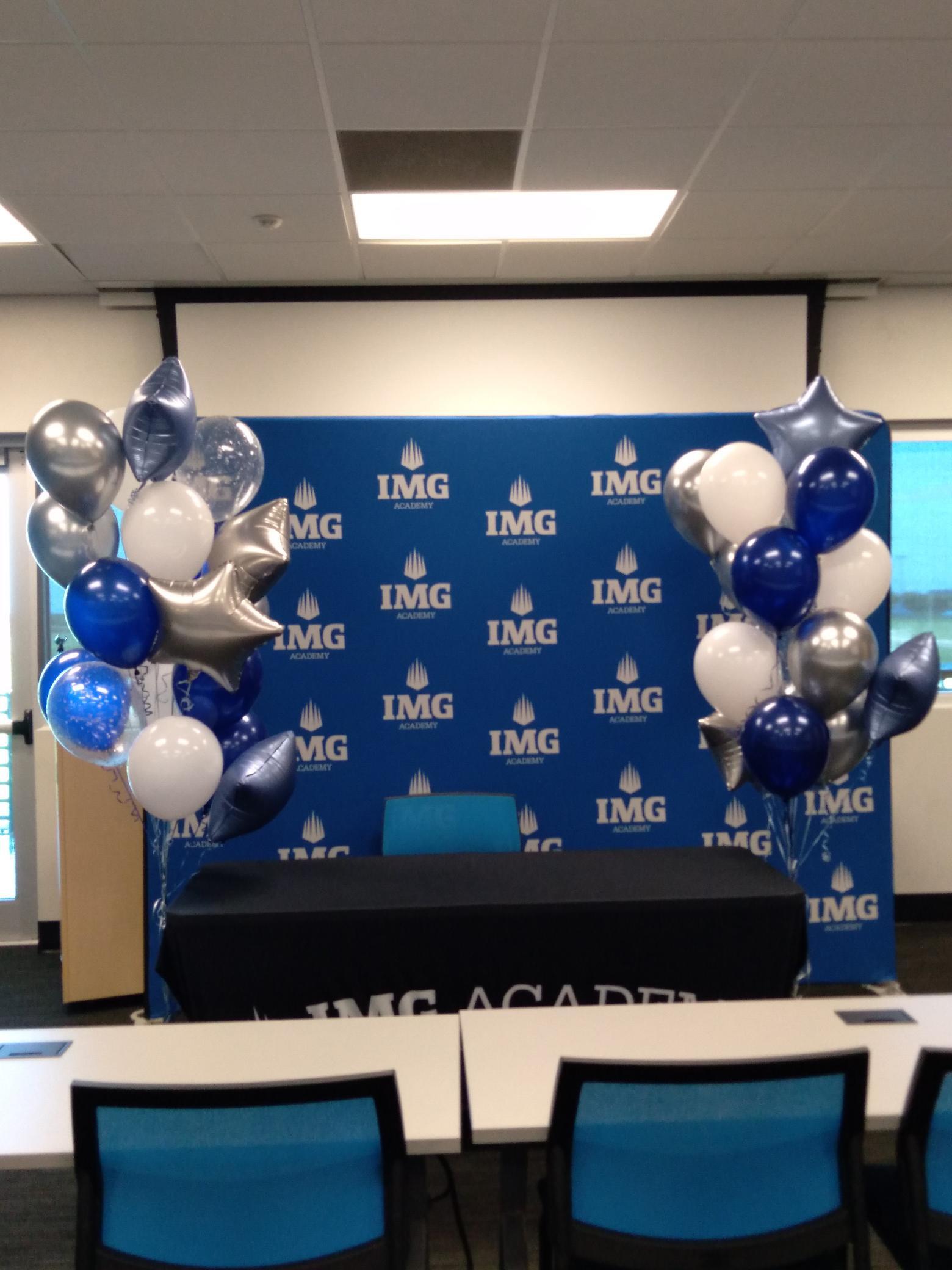 A room with tables and chairs and balloons in front of a wall that says img