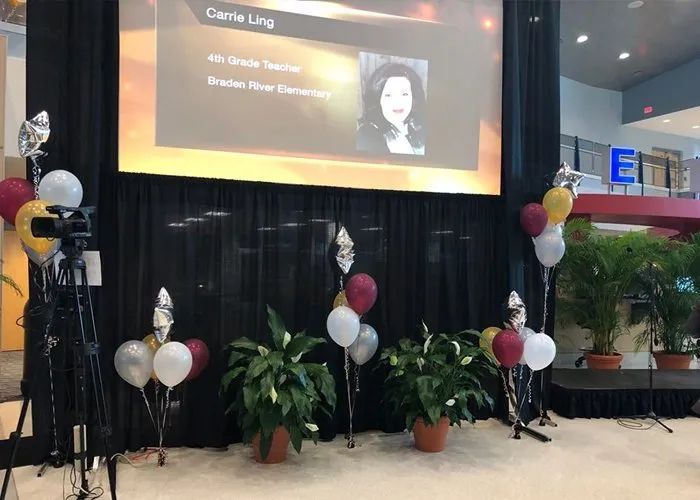 A stage with balloons and plants in front of a large screen