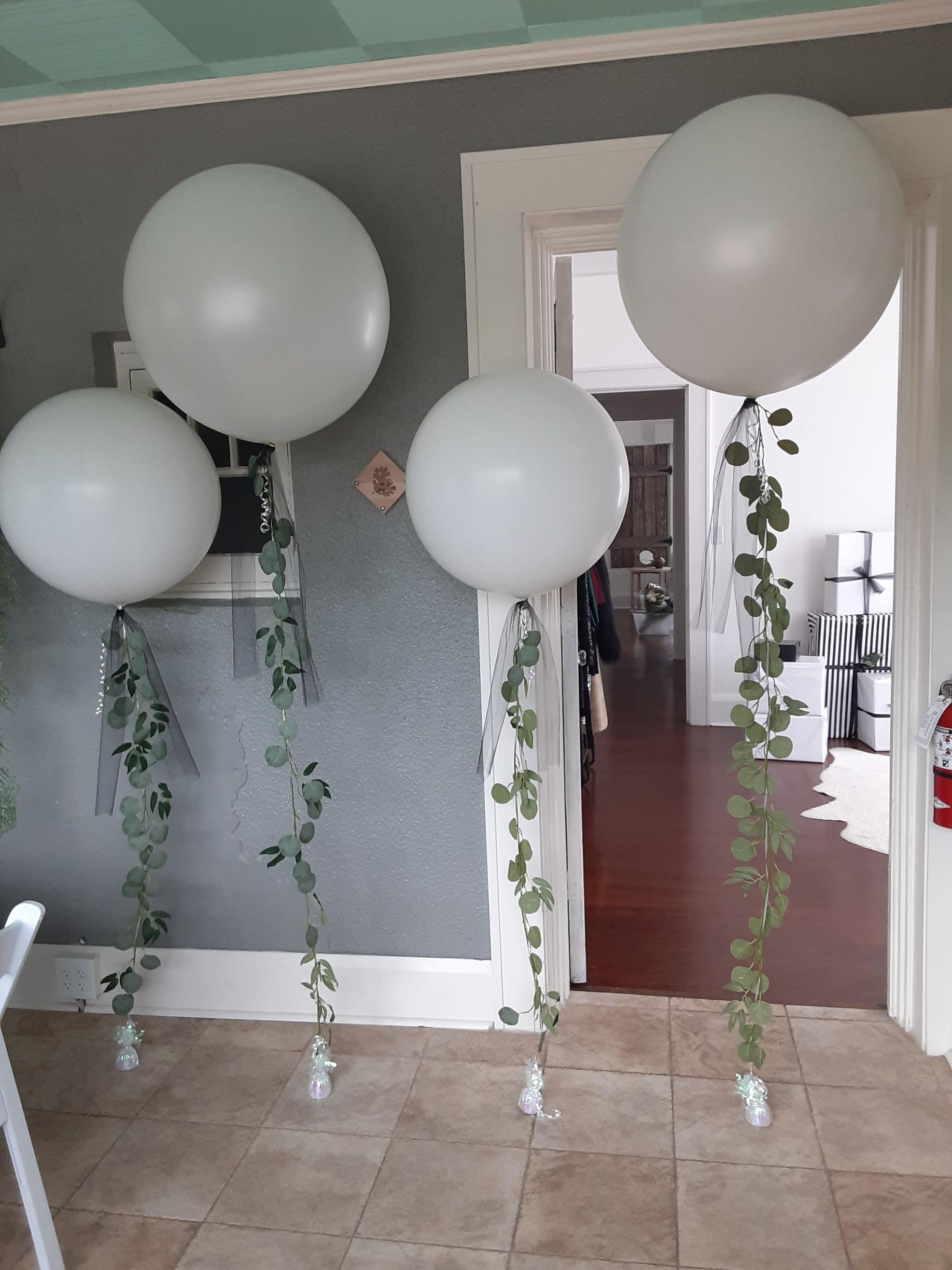 Three white balloons with ivy hanging from them in a room.