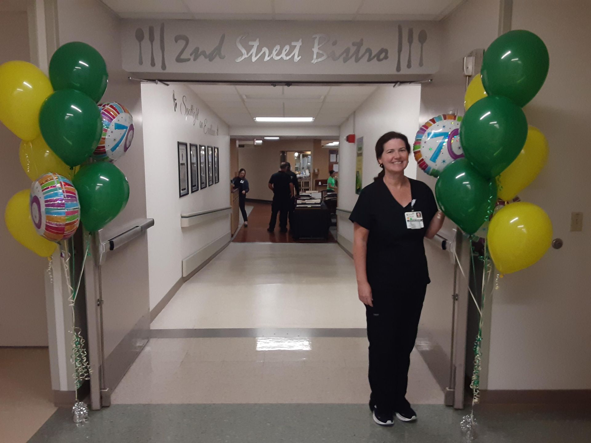 A woman is standing in a hallway with balloons and a sign that says 2nd street bistro