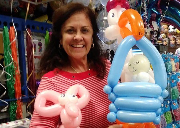 Woman smiles, holding pink balloon elephant and balloon basket with sleeping baby balloon in a shop