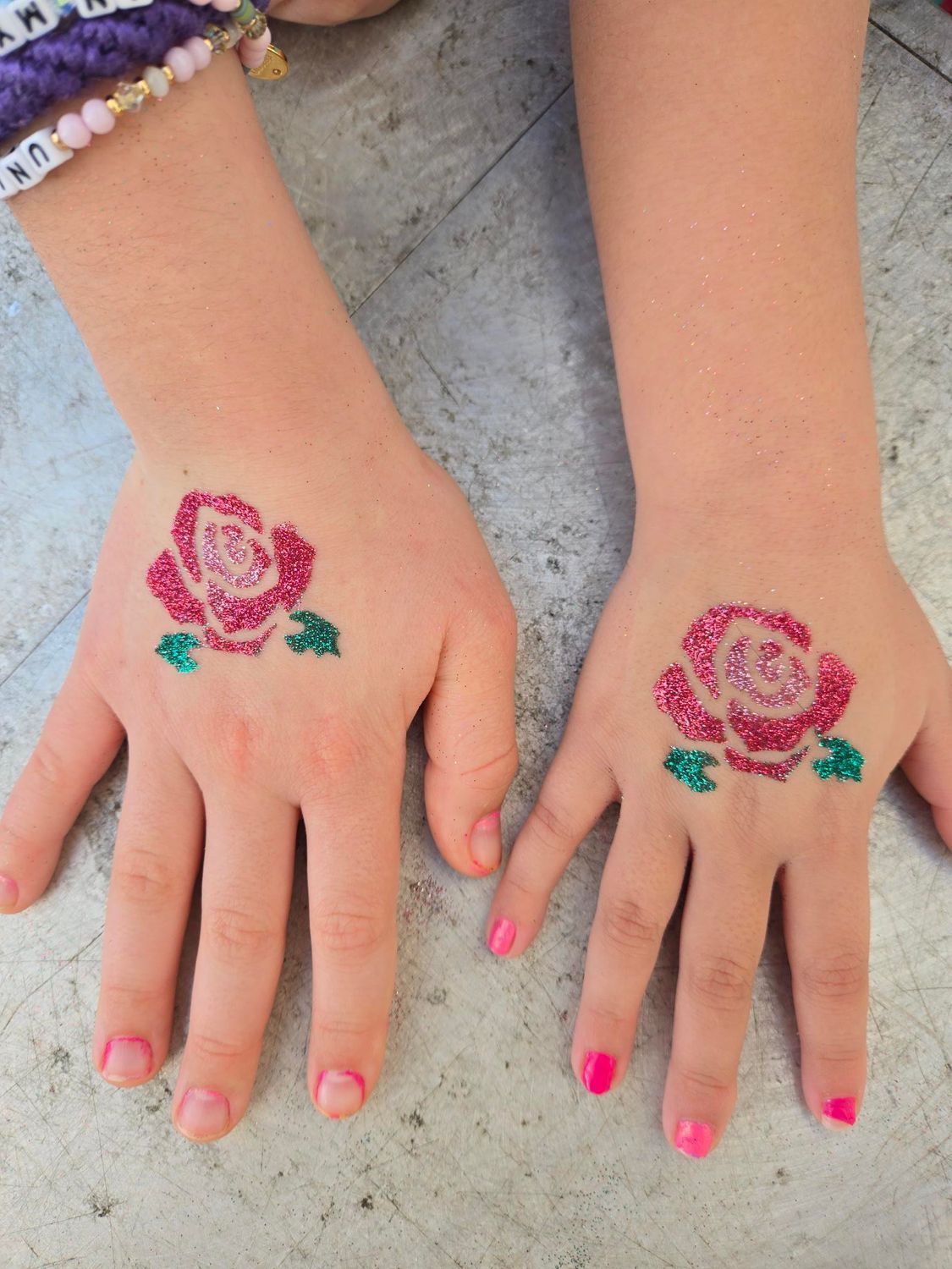 Two small hands with glittery pink rose temporary tattoos.