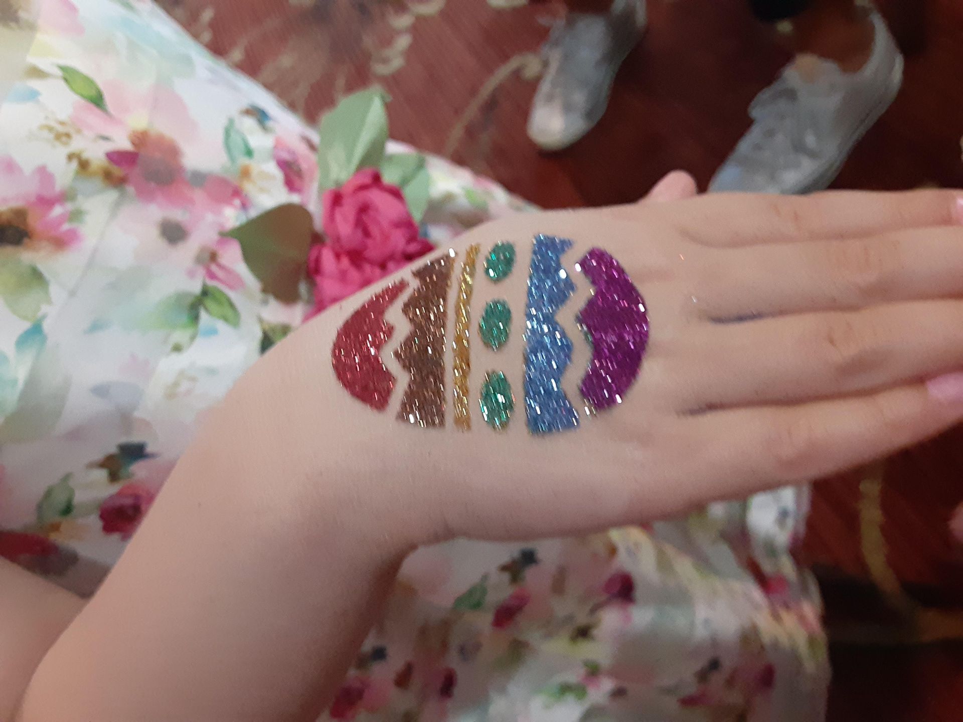 Hand with a glittery Easter egg design, featuring red, gold, green, blue and purple colors.