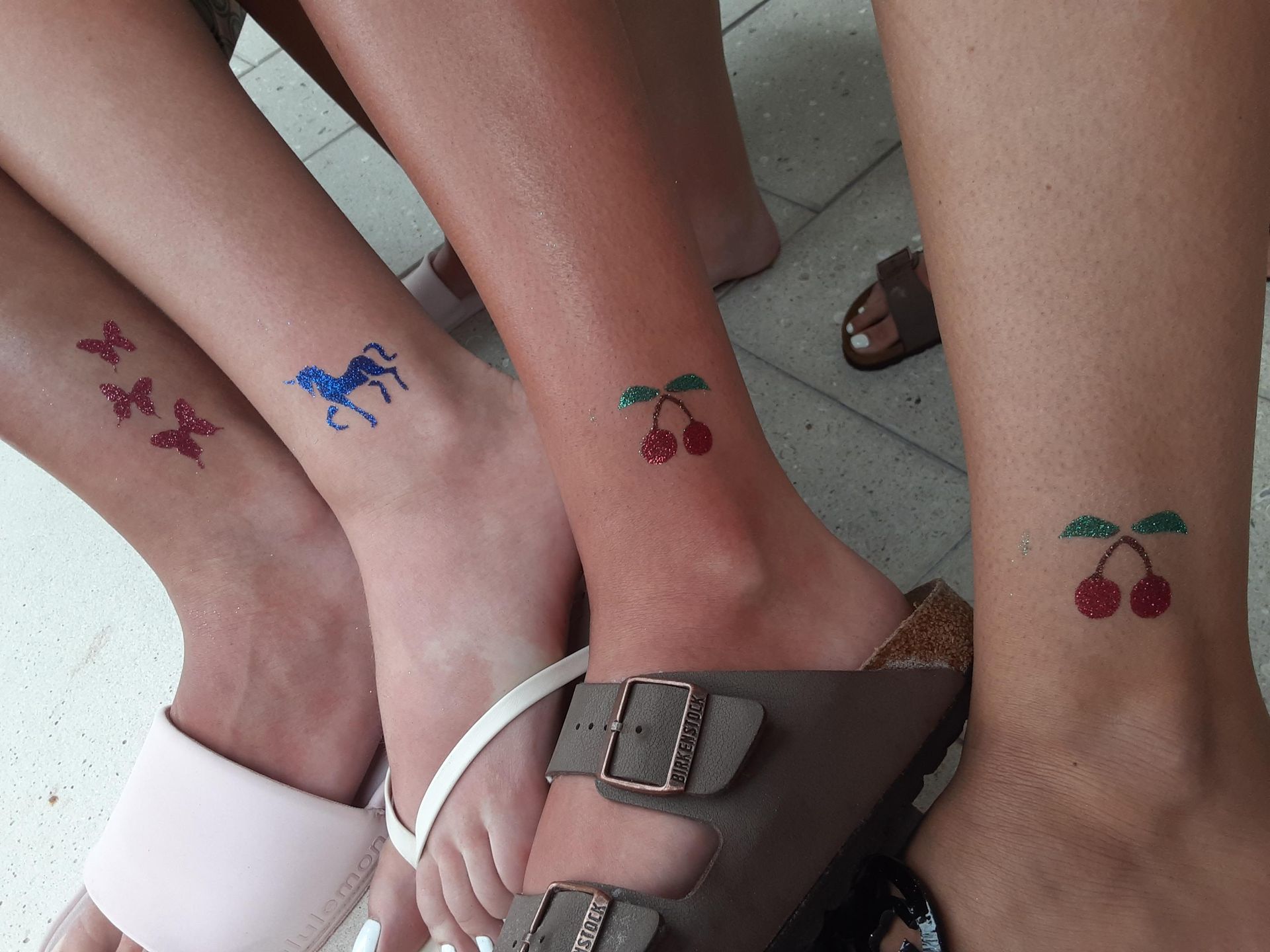 Four people's ankles with temporary tattoos of butterflies, horses, and cherries, in various colors.