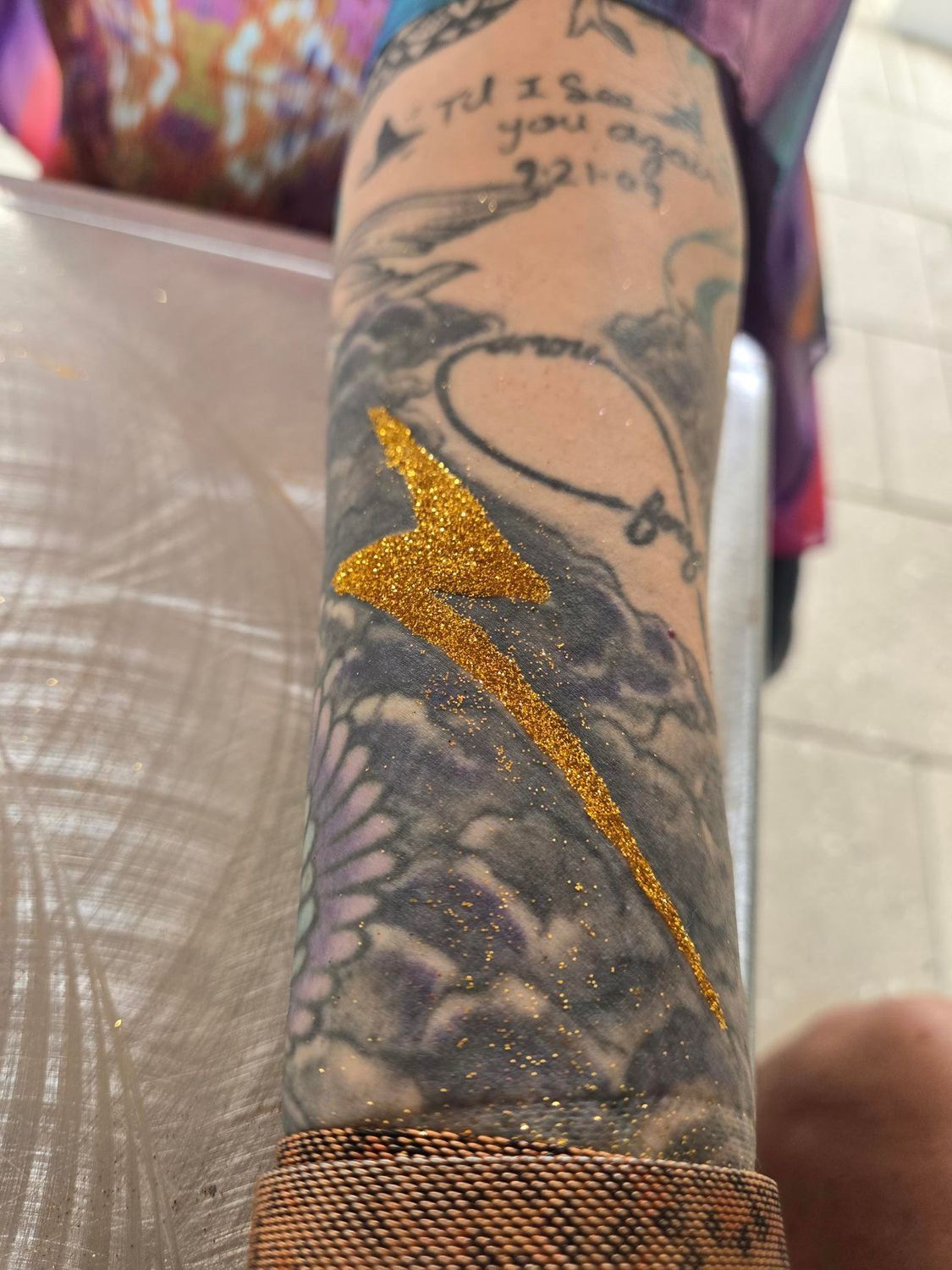 Arm with gold glitter lightning bolt over older tattoos.