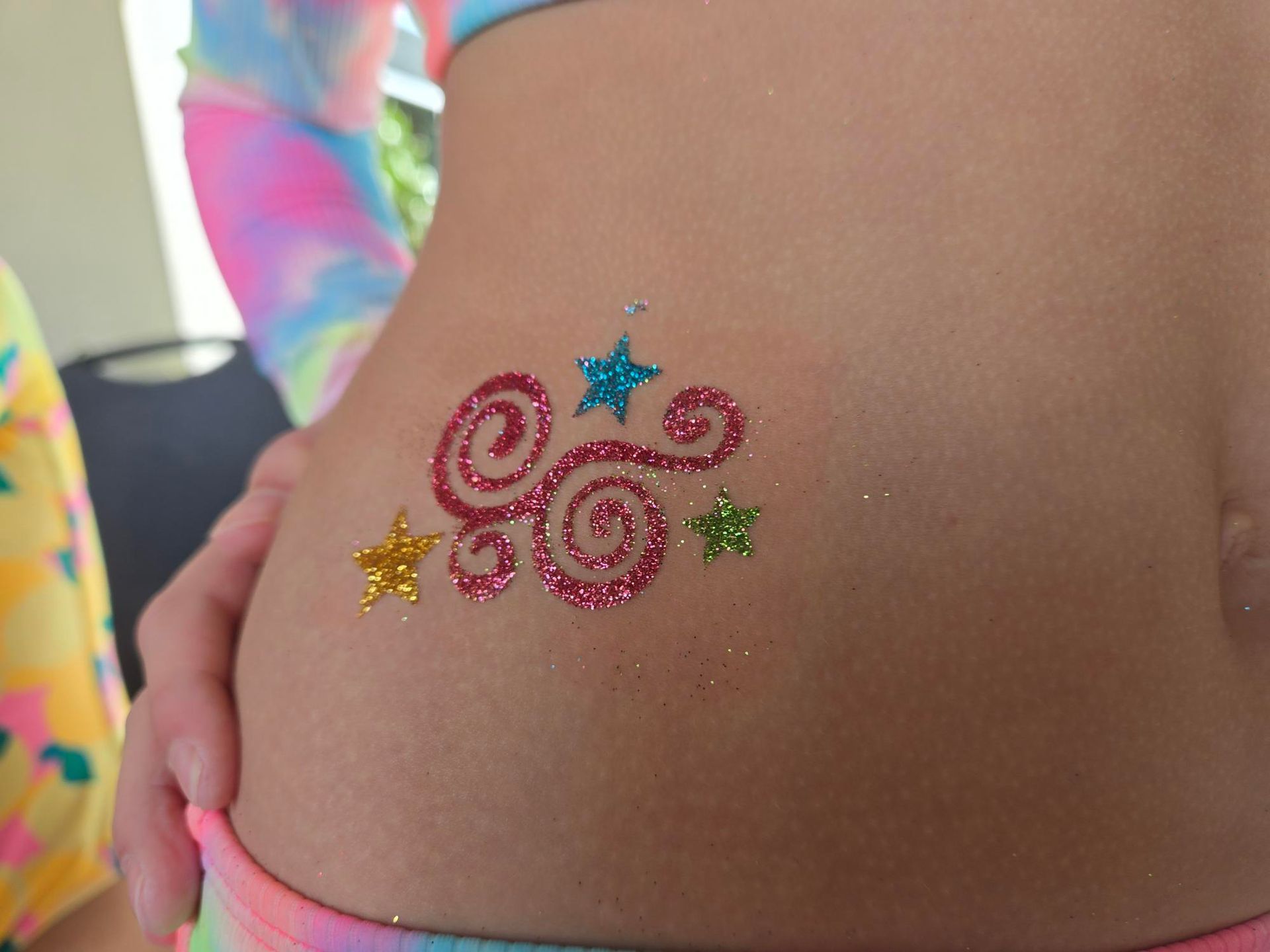 Glitter tattoo of swirling red design and colorful stars on a person's hip.