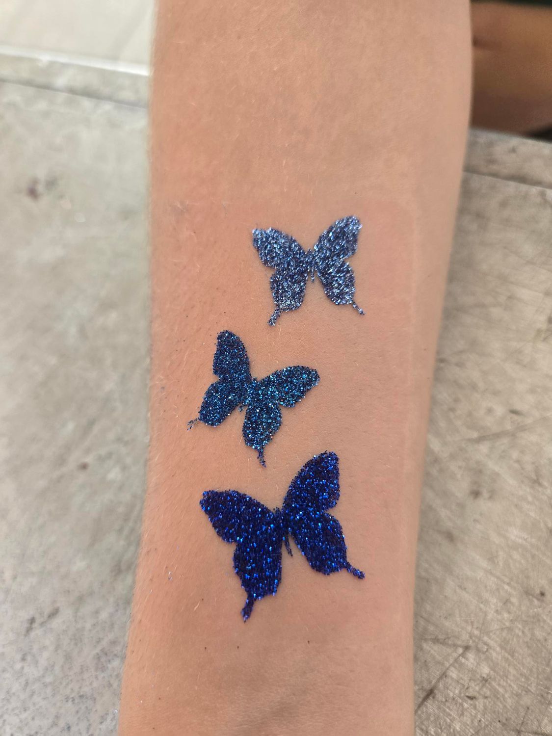 Three blue glitter butterfly temporary tattoos on a person's arm.
