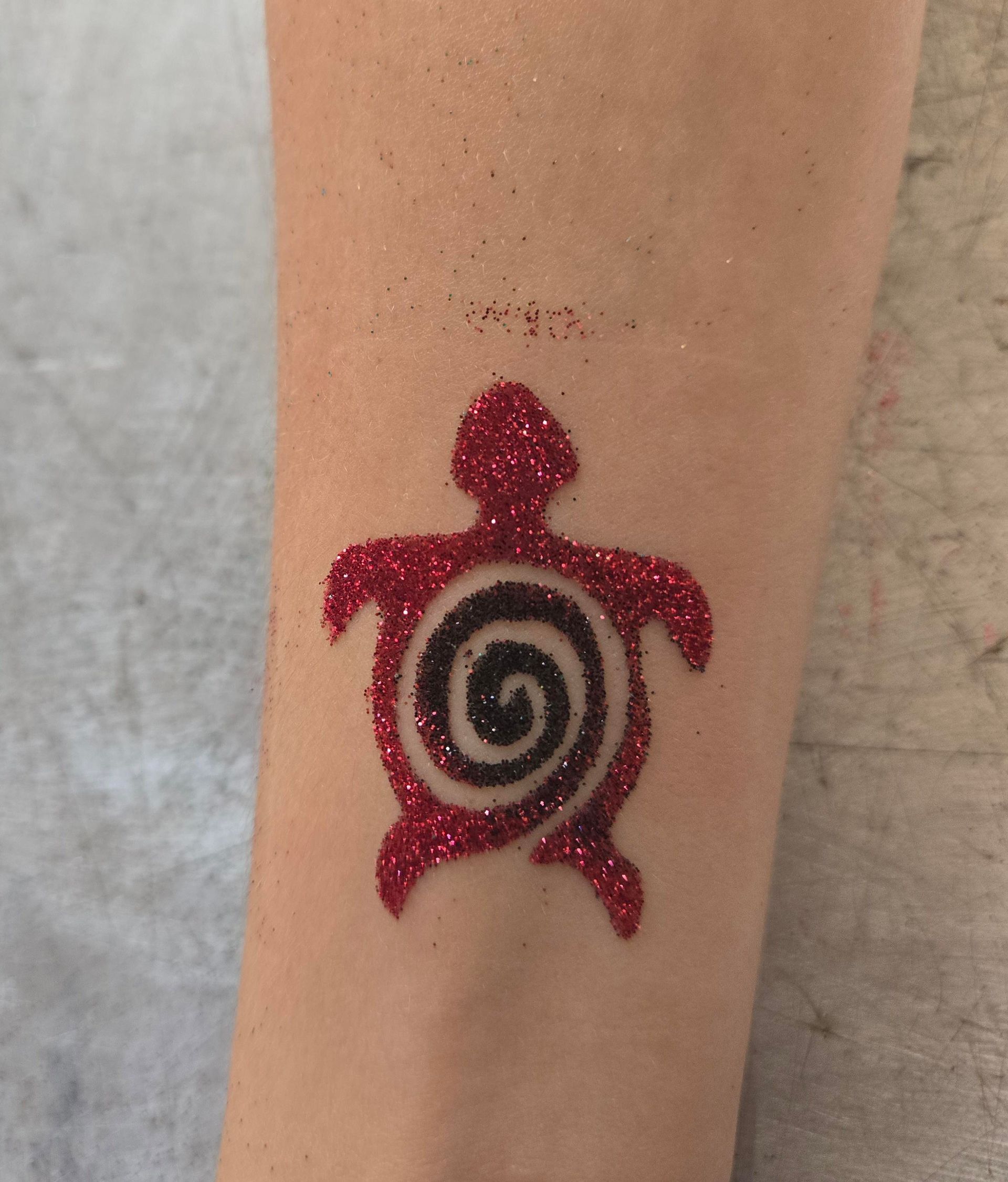Red glitter turtle tattoo with a black spiral center on an arm.