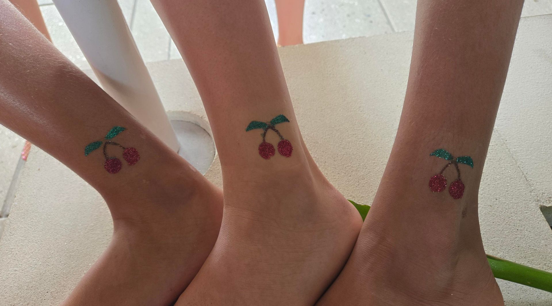 Three ankles with matching cherry tattoos.