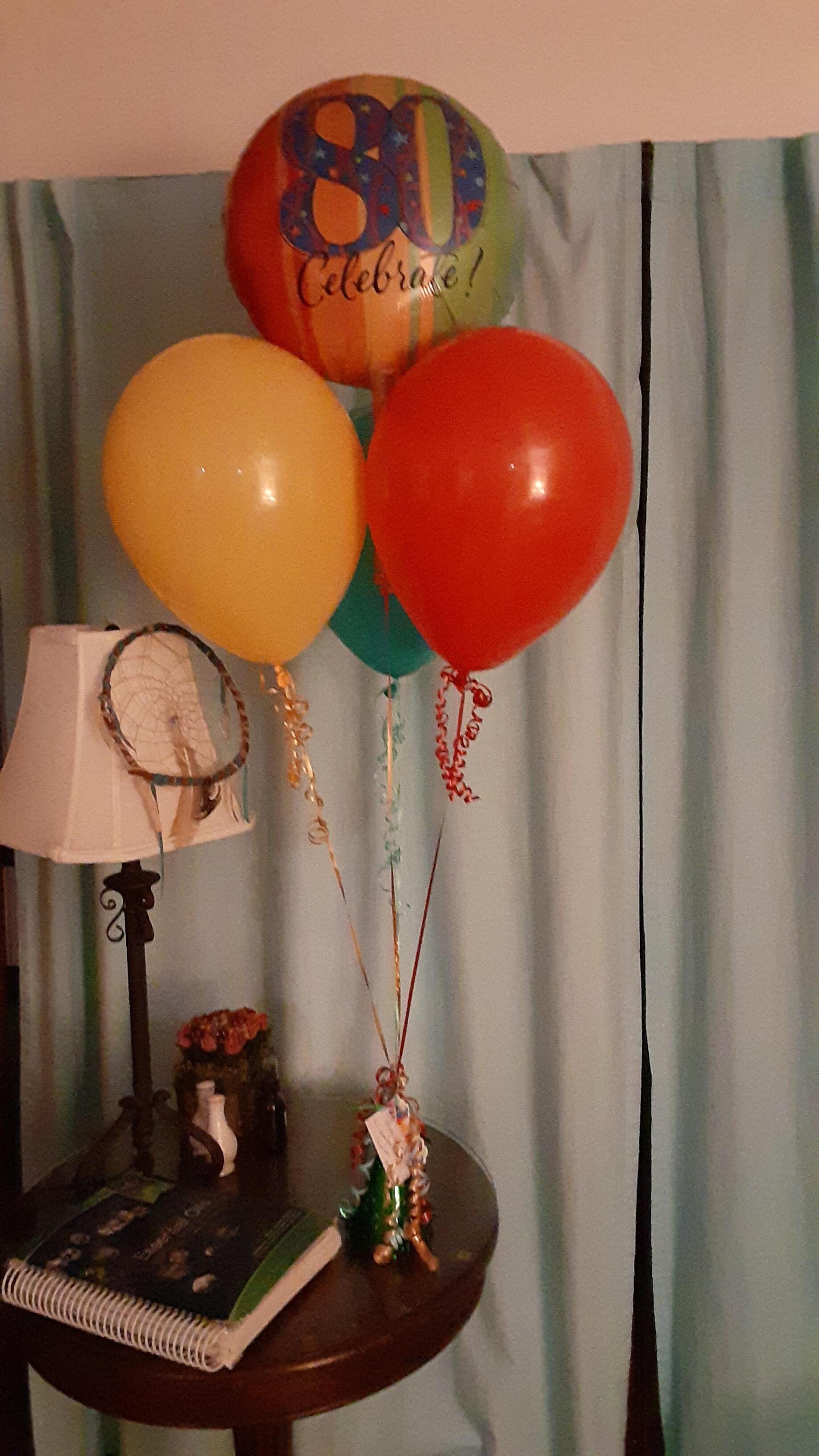 Three balloons on a table with one that says 80