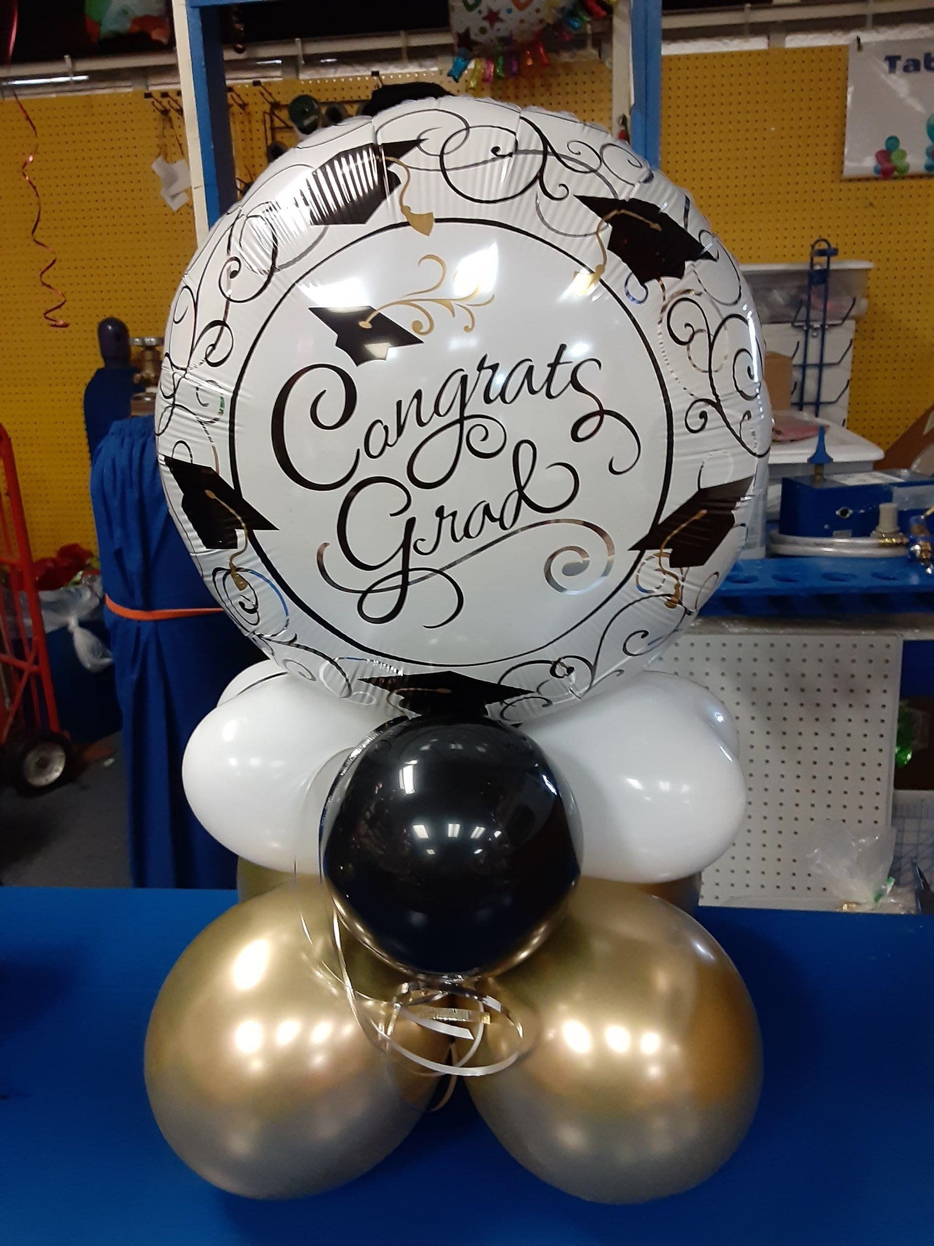 A congratulations graduation balloon is surrounded by black and gold balloons