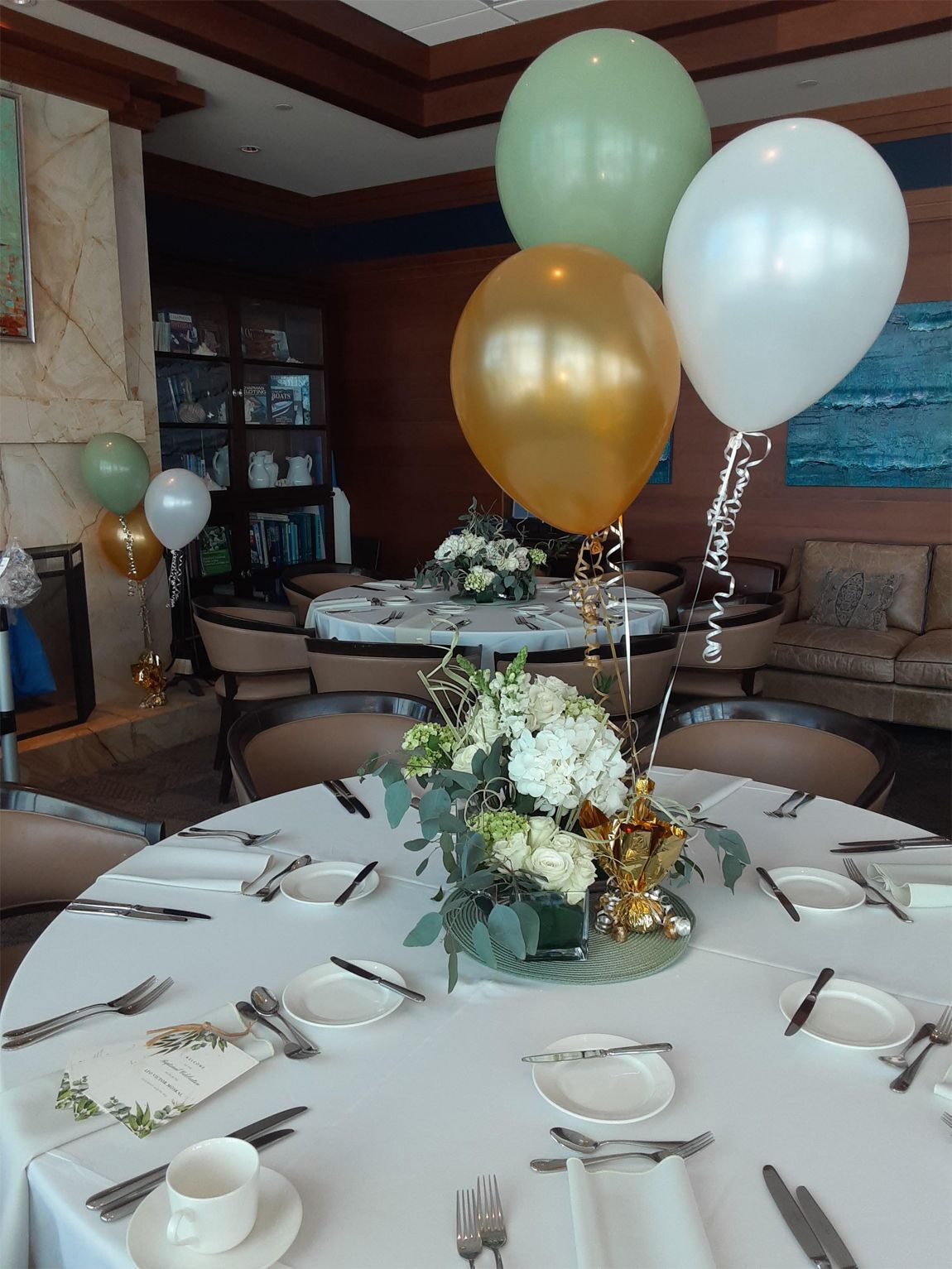 Round table set for a meal with floral centerpiece and balloons; dining room setting.