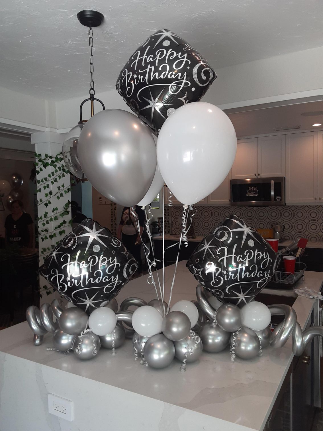 Birthday balloon arrangement on a countertop; black, silver, and white balloons.