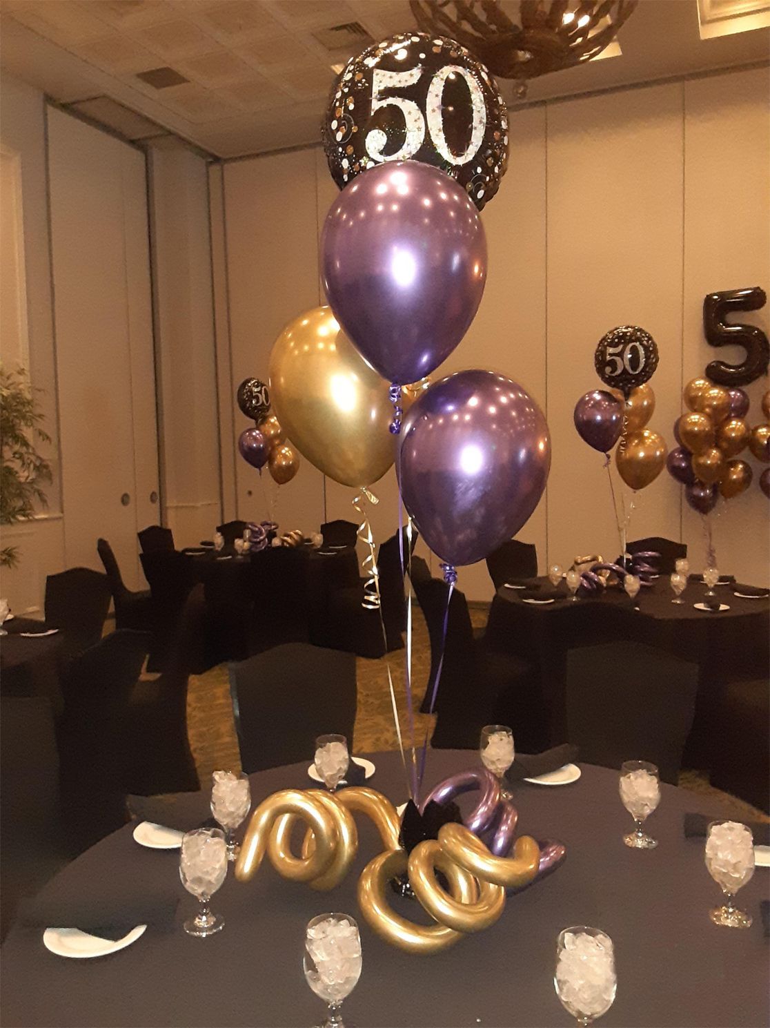 Centerpiece with purple, gold balloons for a 50th birthday. Table setting.