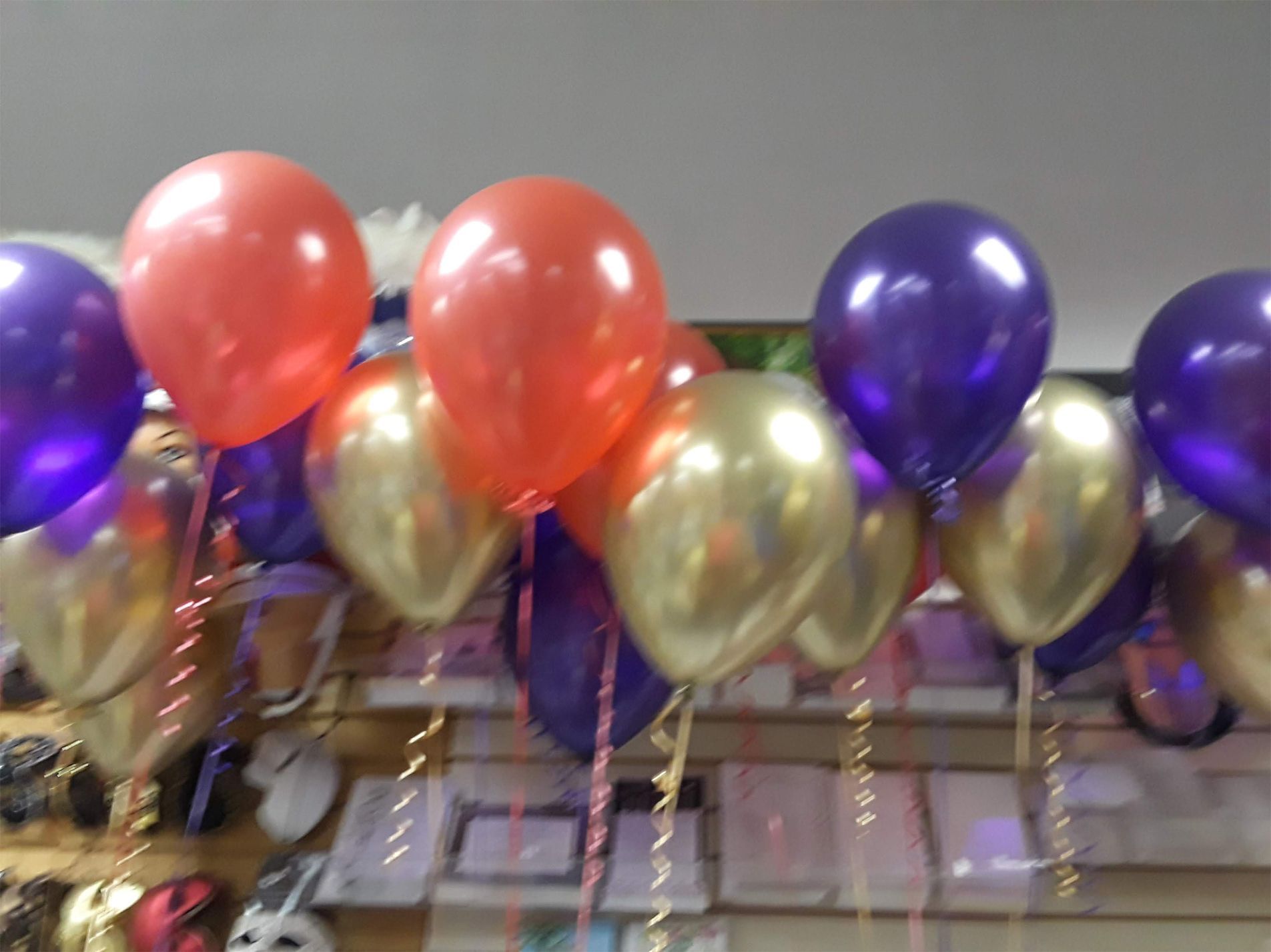 Balloons in various colors (purple, orange, gold) displayed indoors, likely for a celebration.